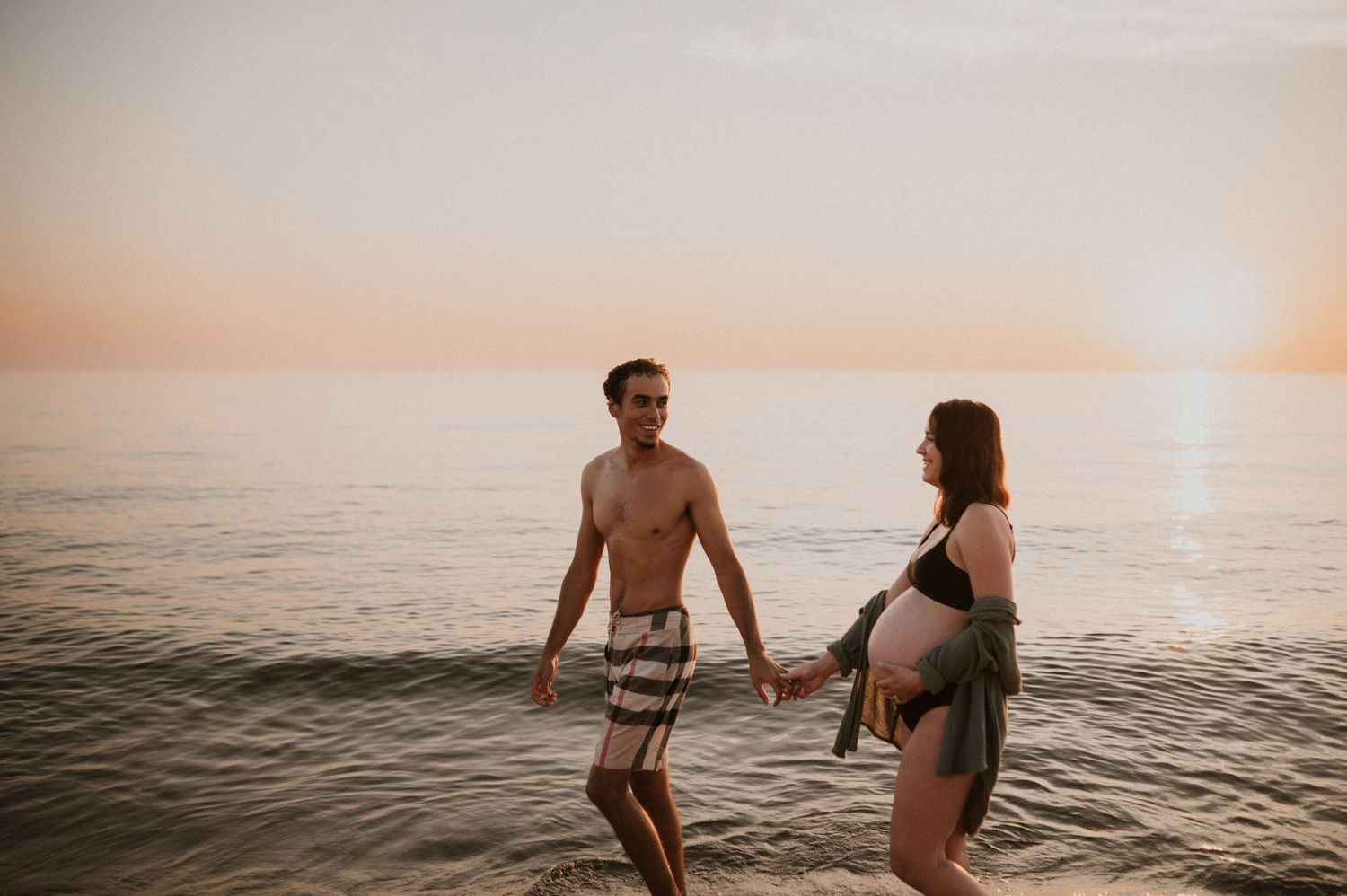 Couple holding hands while standing in ocean water during golden hour sunset.