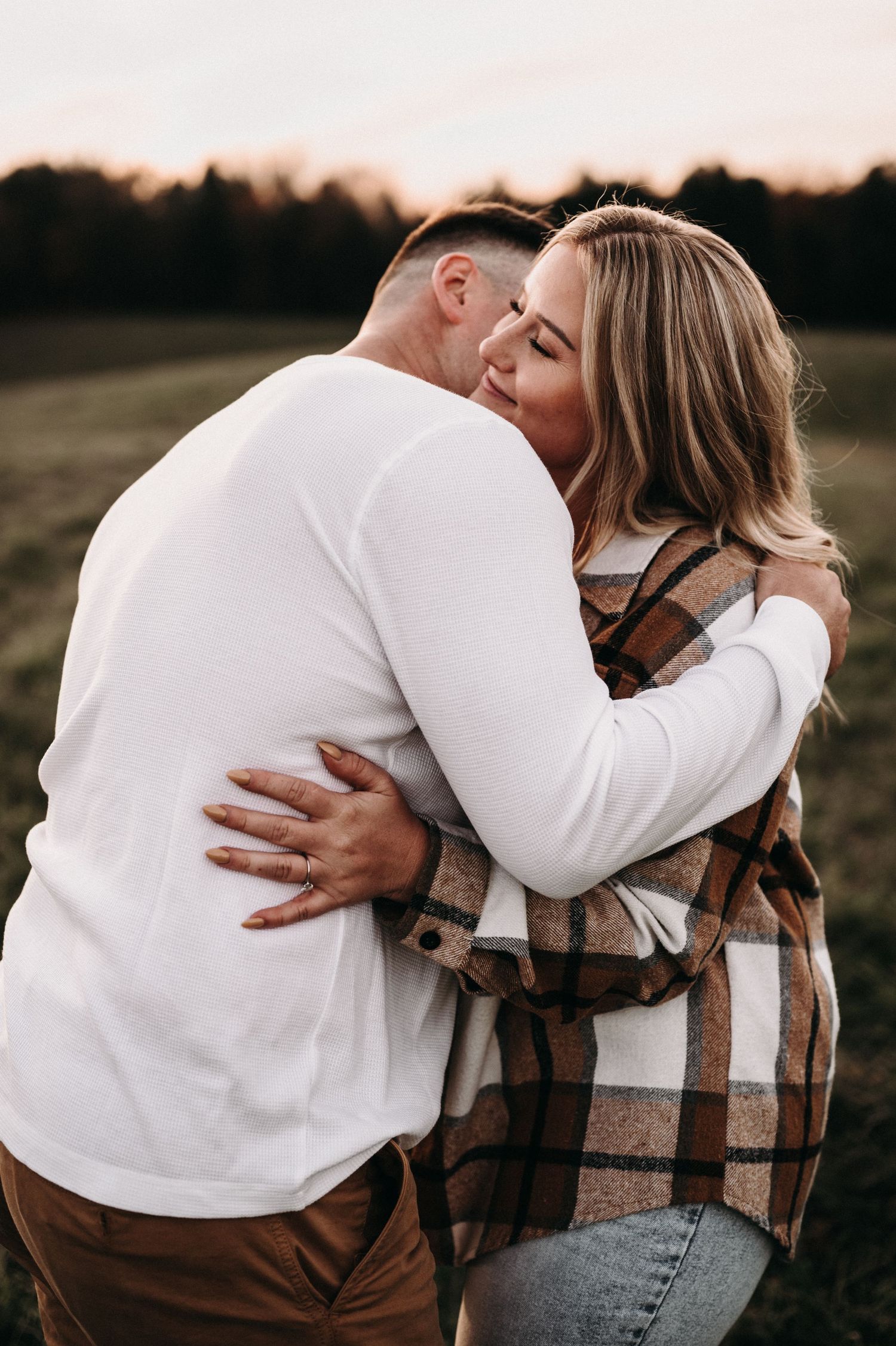 Intimate embrace between couple wearing casual fall clothing in sunset field.