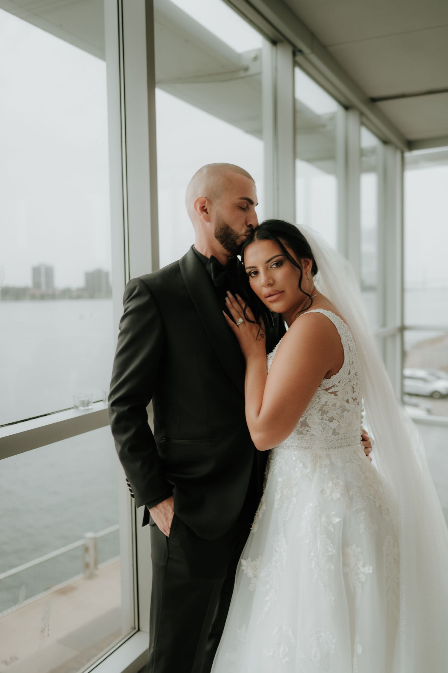 Intimate wedding portraits by large windows with soft natural lighting.
