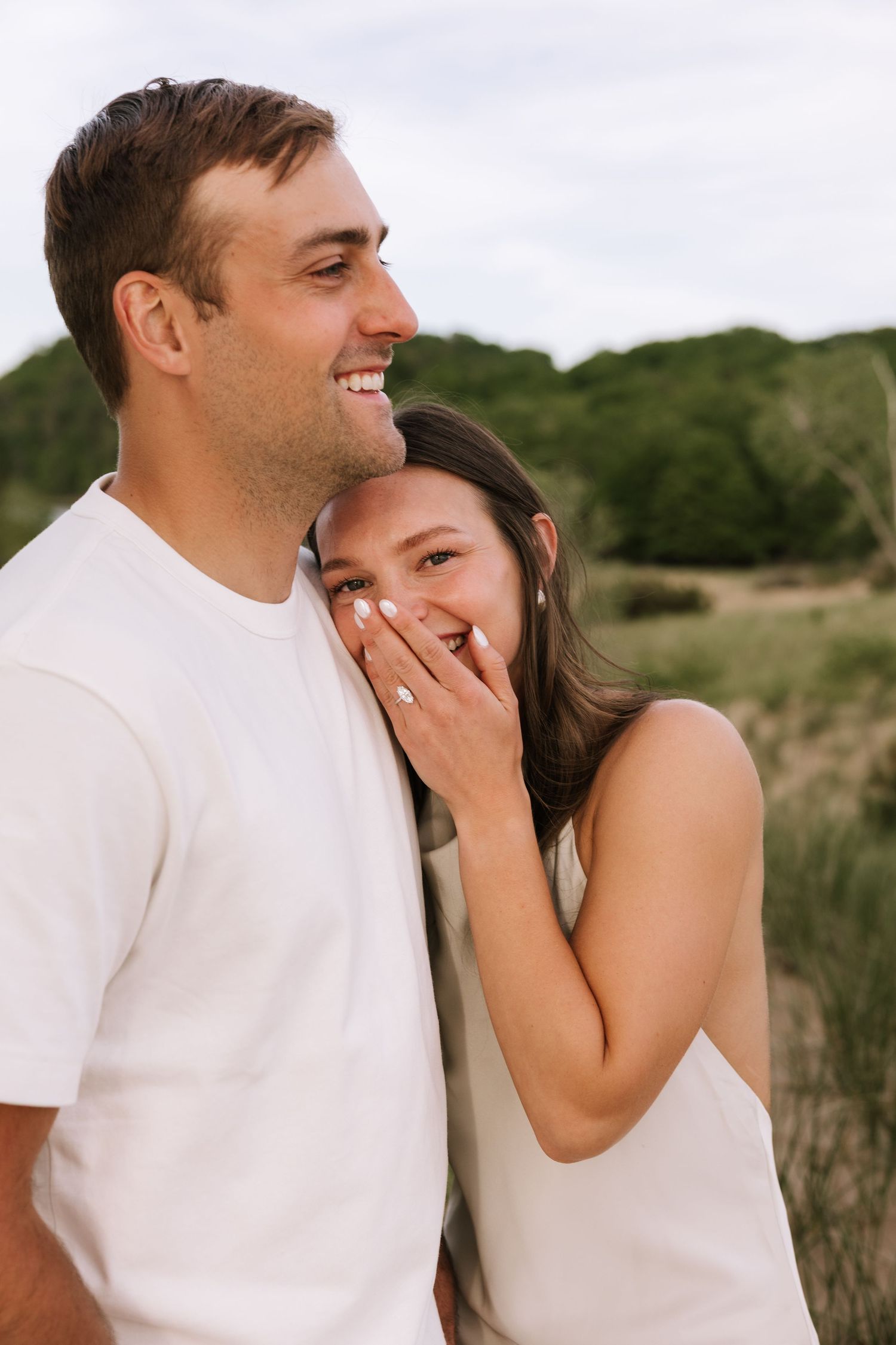 Happy couple laughing together outdoors, woman covering her smile while man in white tee grins broadly.