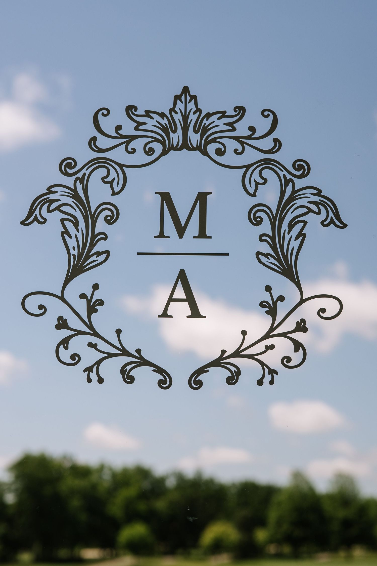 Decorative monogram letters M and A with ornate flourishes against a blue sky background.