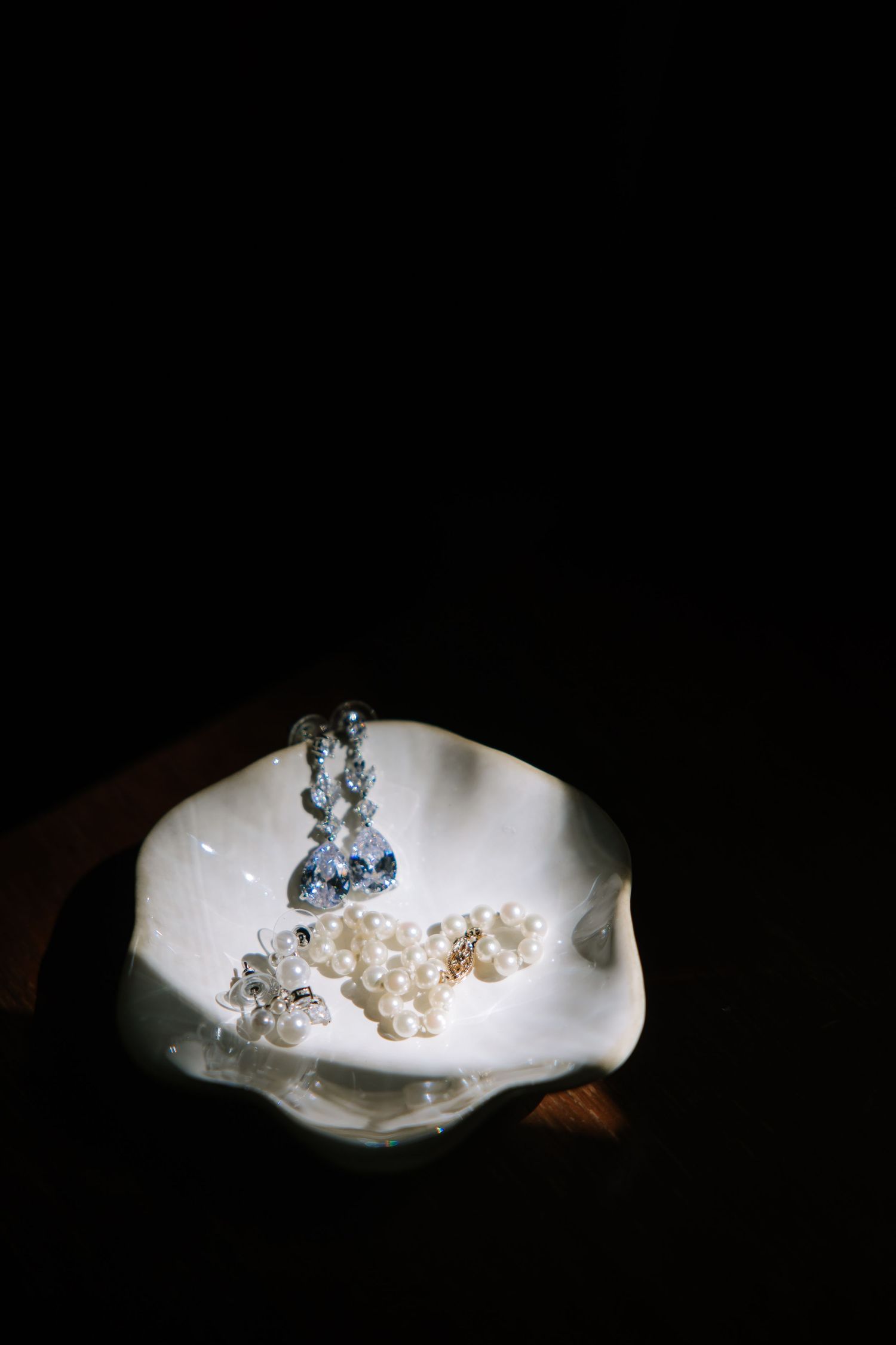 Delicate crystal jewelry pieces displayed on white surface with dramatic lighting.