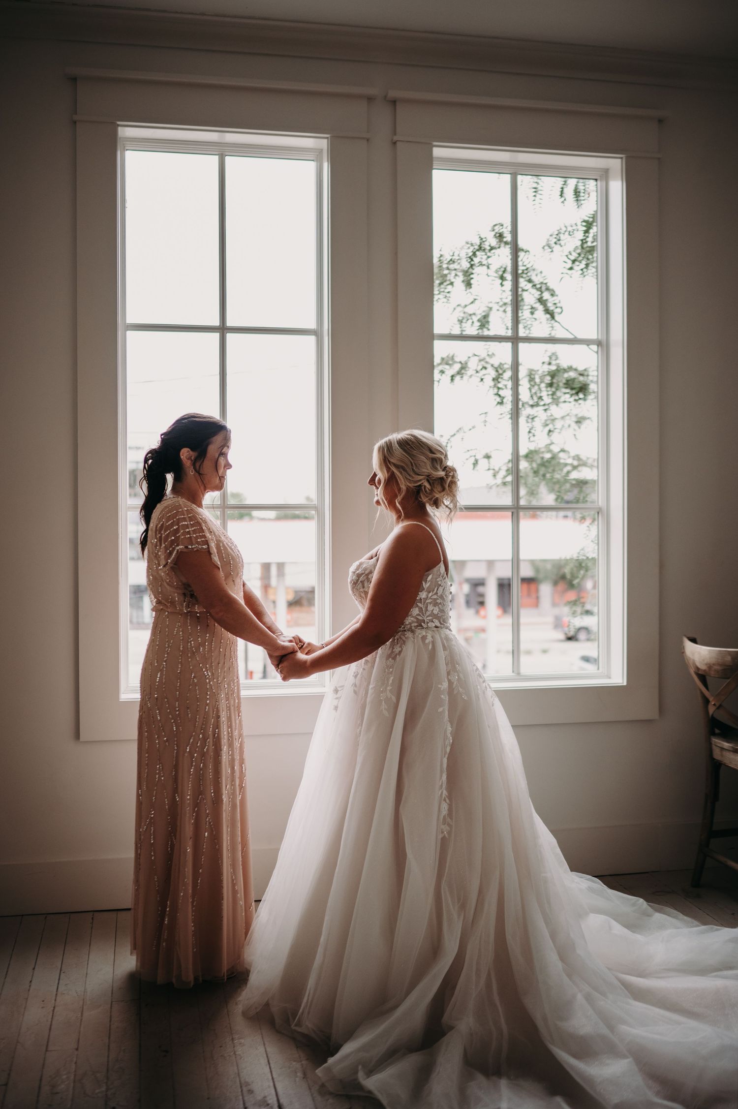 Intimate wedding moment between two people in formal attire by sunlit windows.