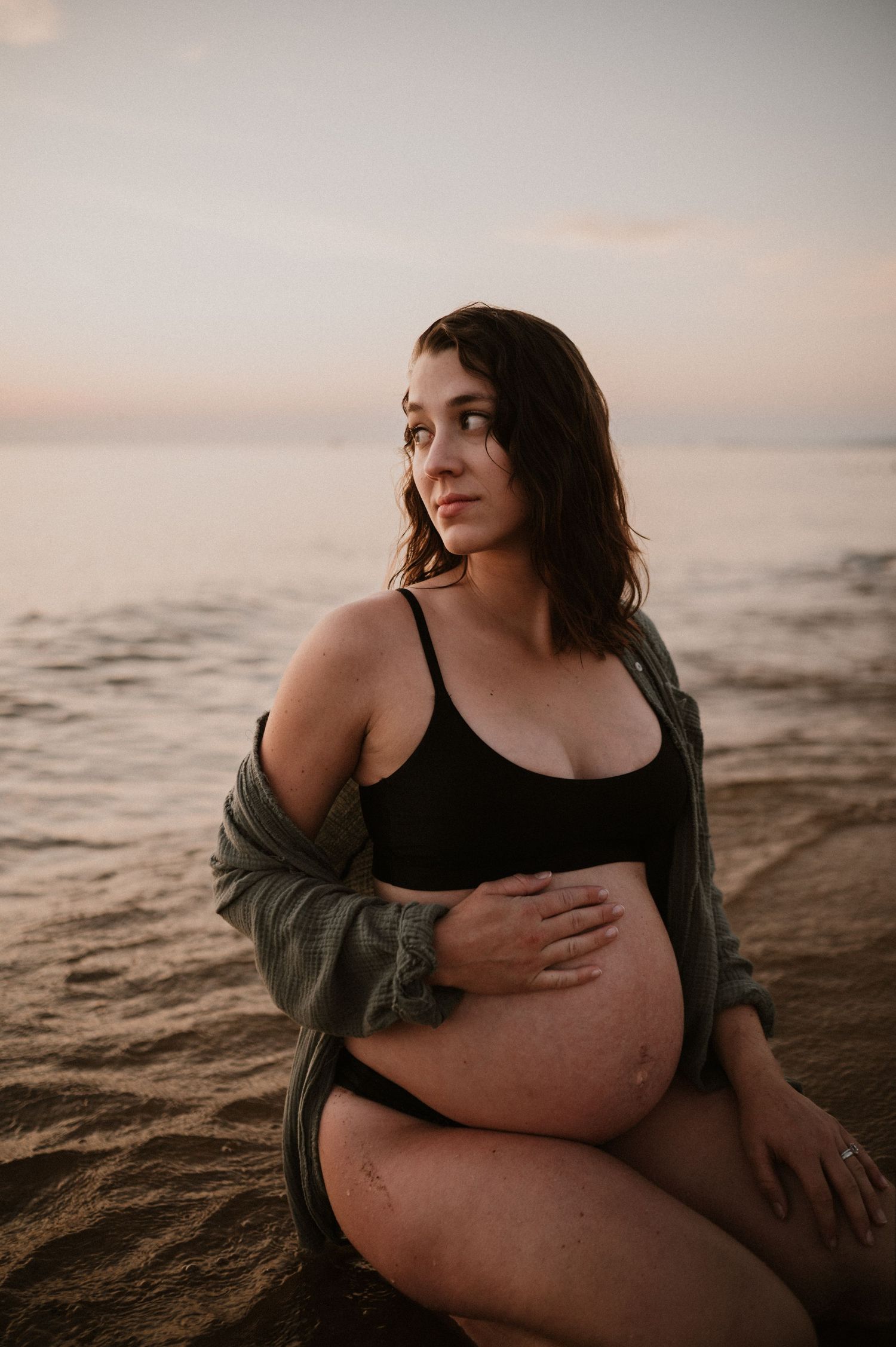 Artistic maternity photo of expectant mother in black swimwear on beach at dusk.