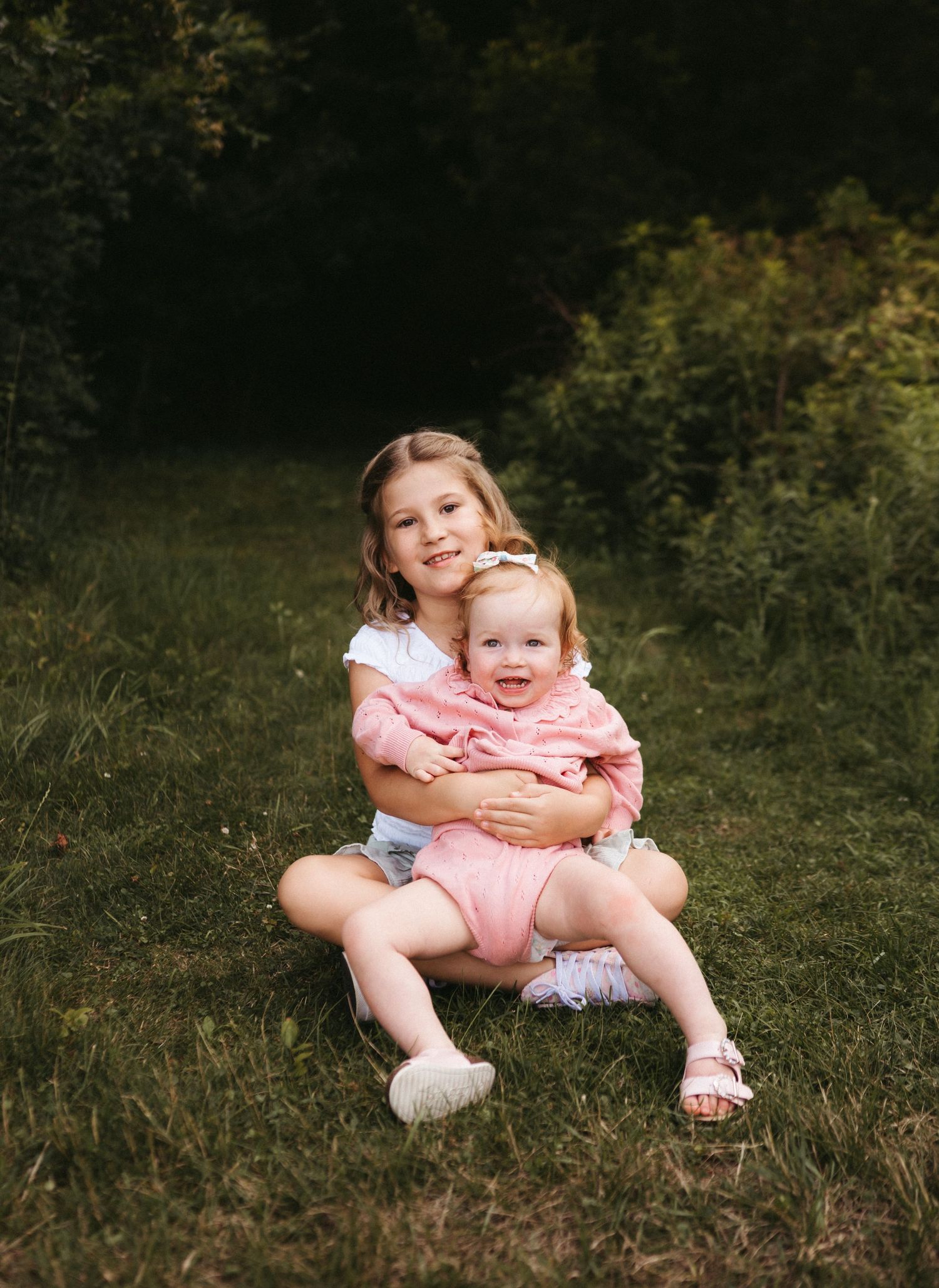 Two children in matching pink outfits sit together on grass outdoors.