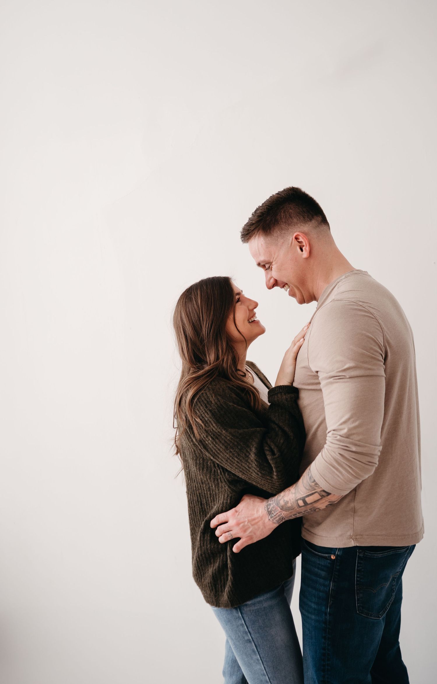 Couple laughing together in casual wear against white backdrop.