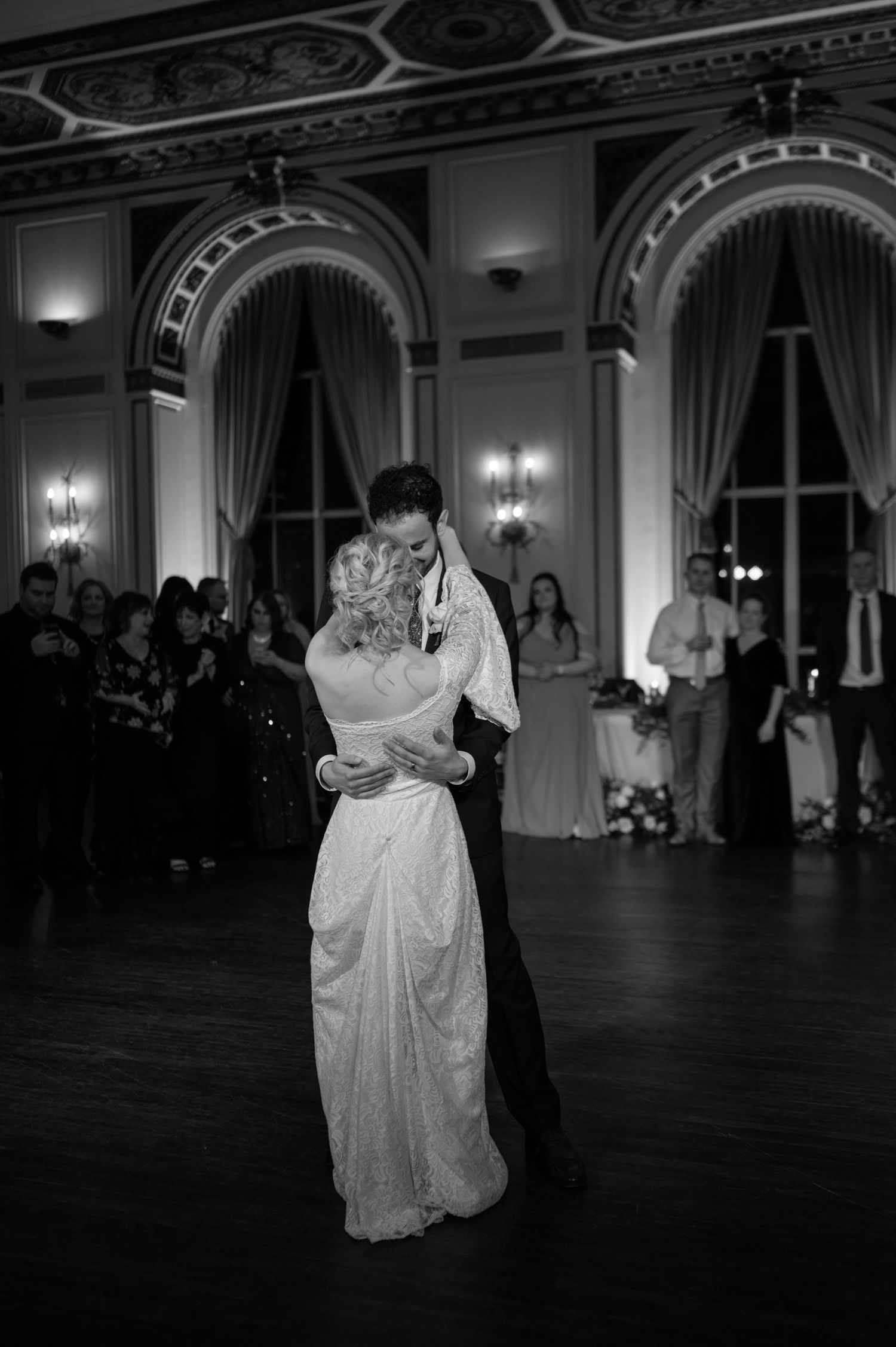 Black and white photos of couple's first dance in grand ballroom with ornate architecture.