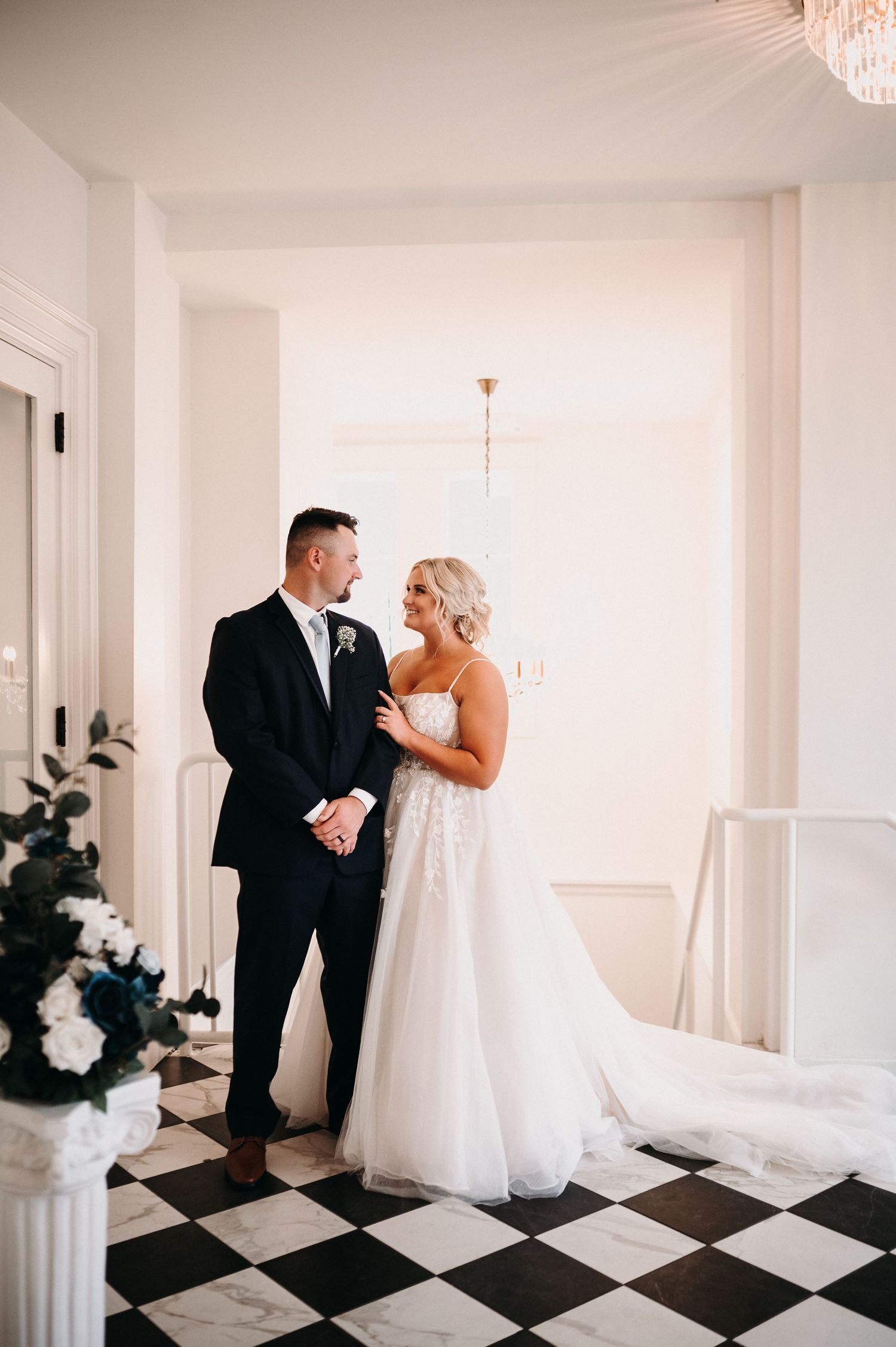 A couple shares an intimate moment on a black and white checkered floor in an elegant white interior.