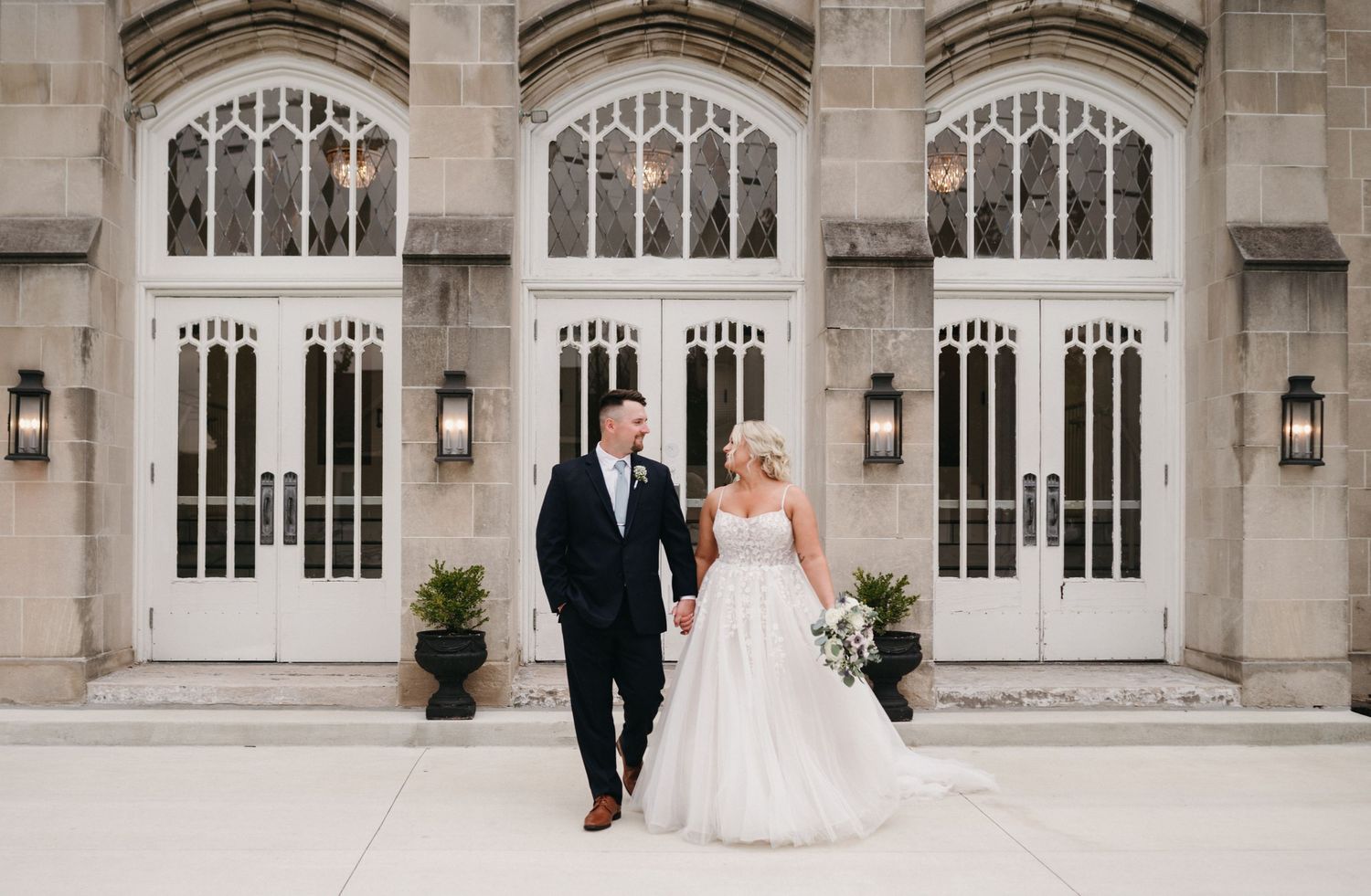 Couple walking together in front of elegant white Gothic church doors.