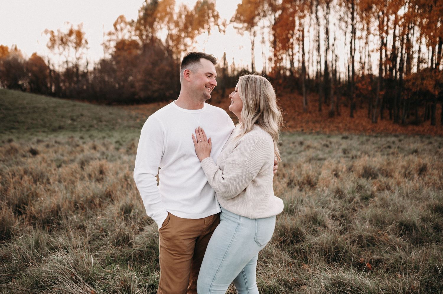 Couple in matching white sweaters share intimate moment in rustic fall setting.