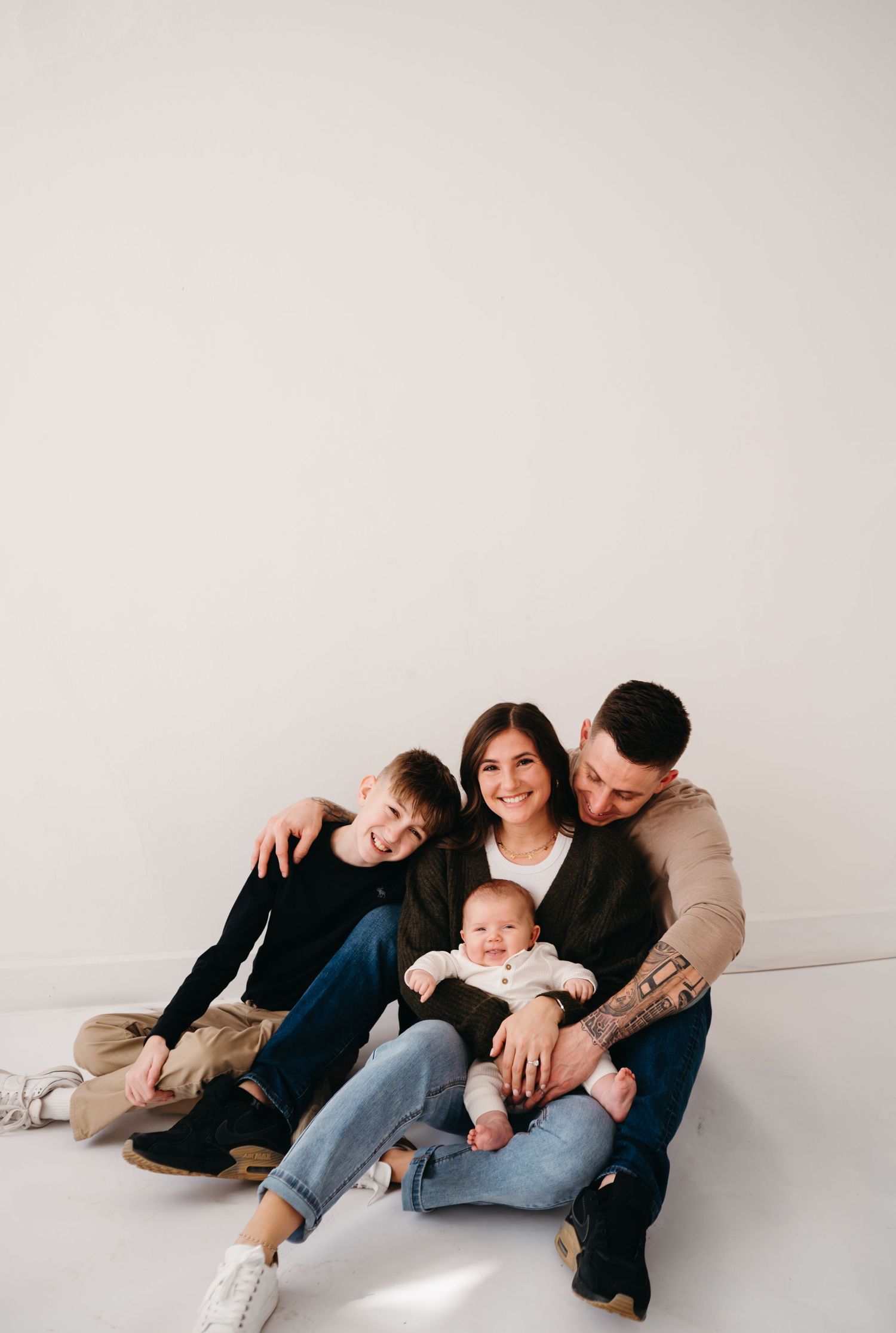 Casual family portrait with everyone sitting together on white floor sharing intimate moment.