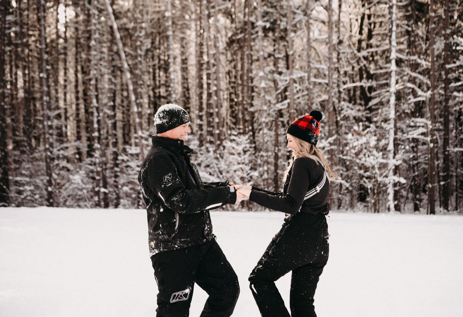 Two people playfully holding hands while enjoying a snowy winter forest adventure.