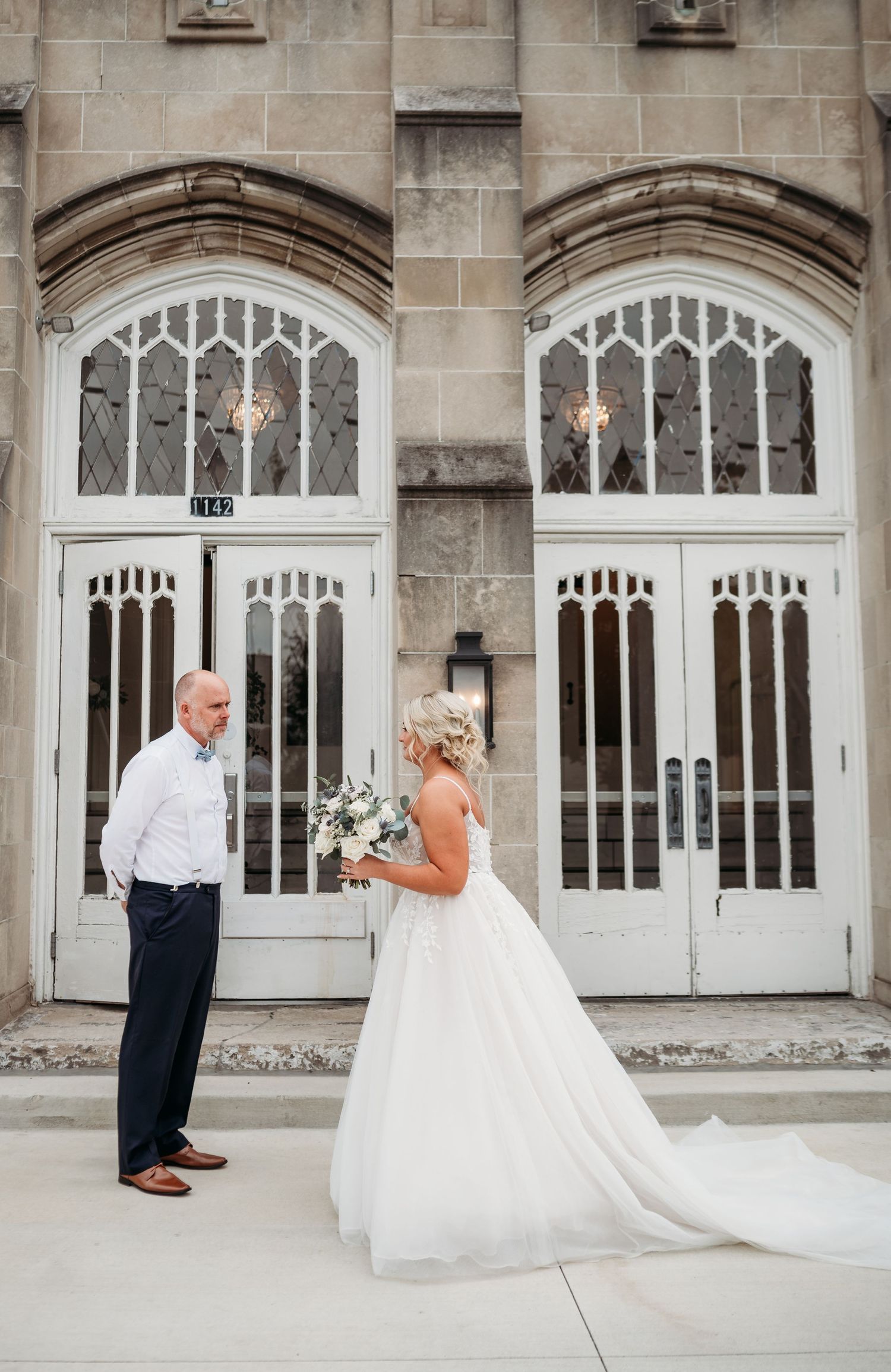 An elegant wedding scene in front of a historic church entrance with gothic-style white doors.
