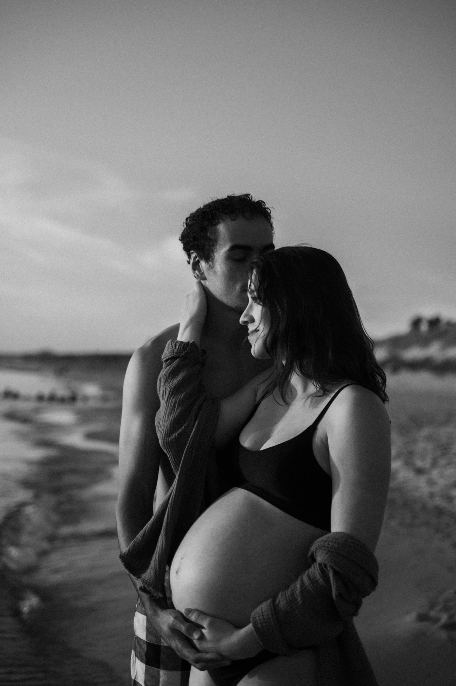 Black and white maternity beach photo showing an intimate moment during pregnancy.