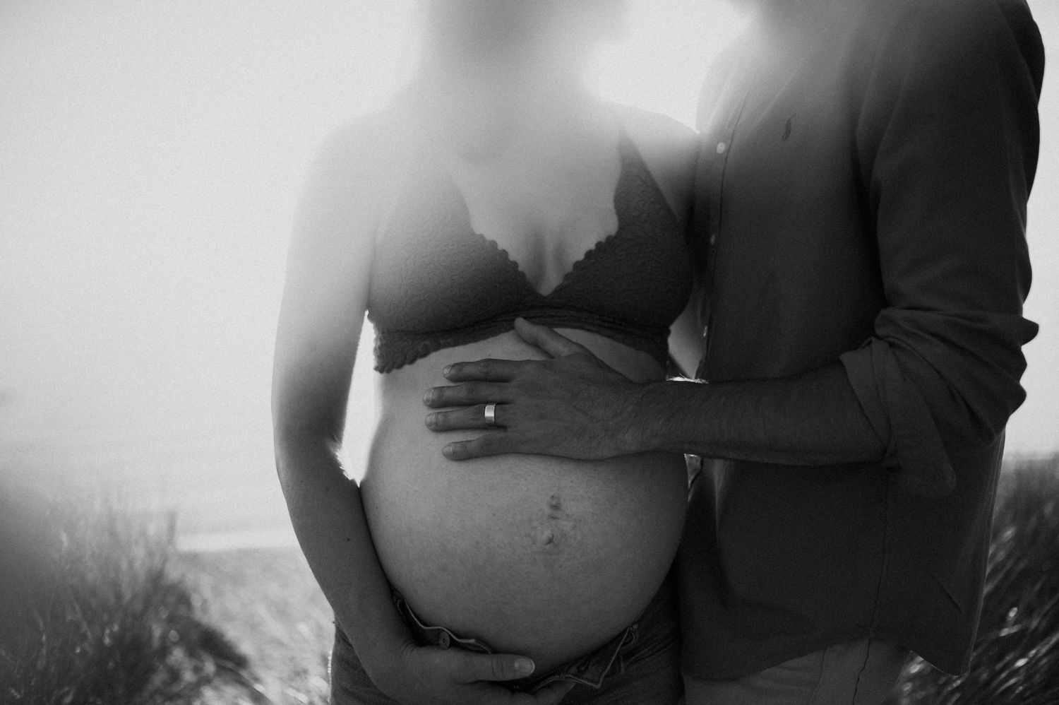 Black and white intimate maternity portrait showing gentle embrace and baby bump.