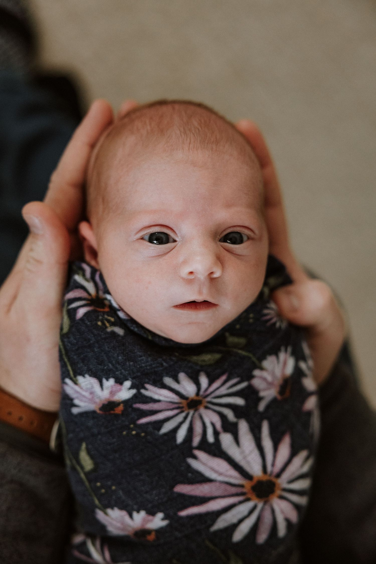 A newborn baby wearing a black floral print swaddle blanket with pink daisy patterns.
