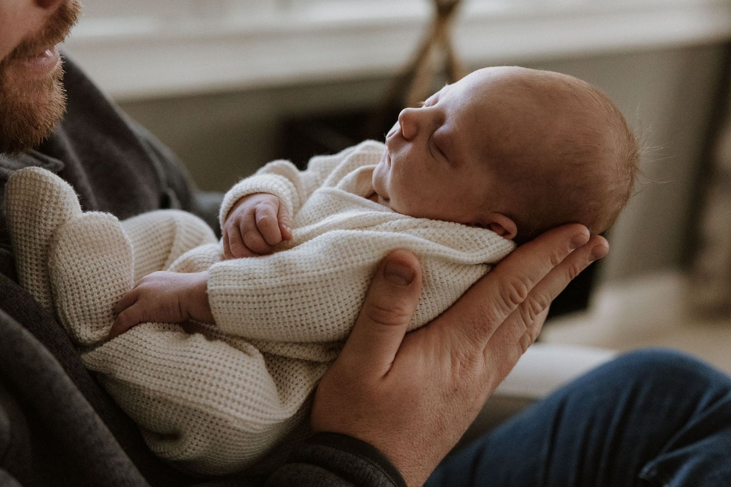 A sleeping newborn in white clothing being cradled in gentle hands.