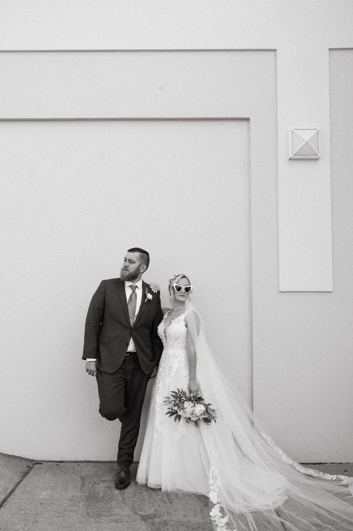 Minimalist wedding portraits against a white wall showcase elegant bridal attire.