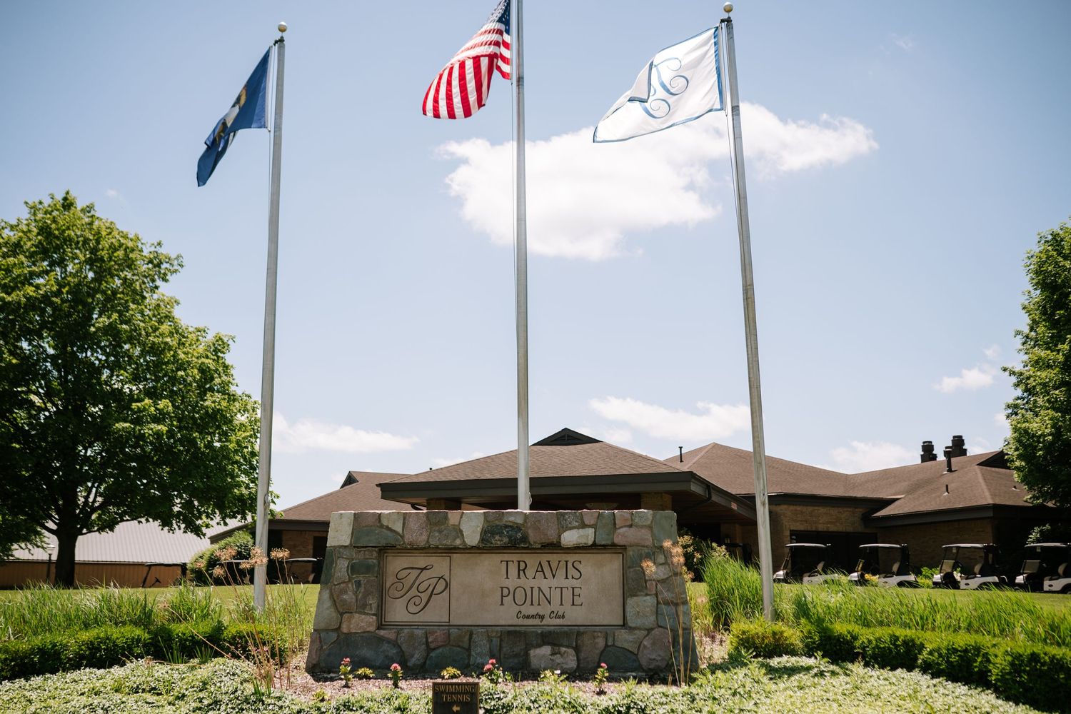 Exterior view of a golf club building with American flags flying on flagpoles against a blue sky.