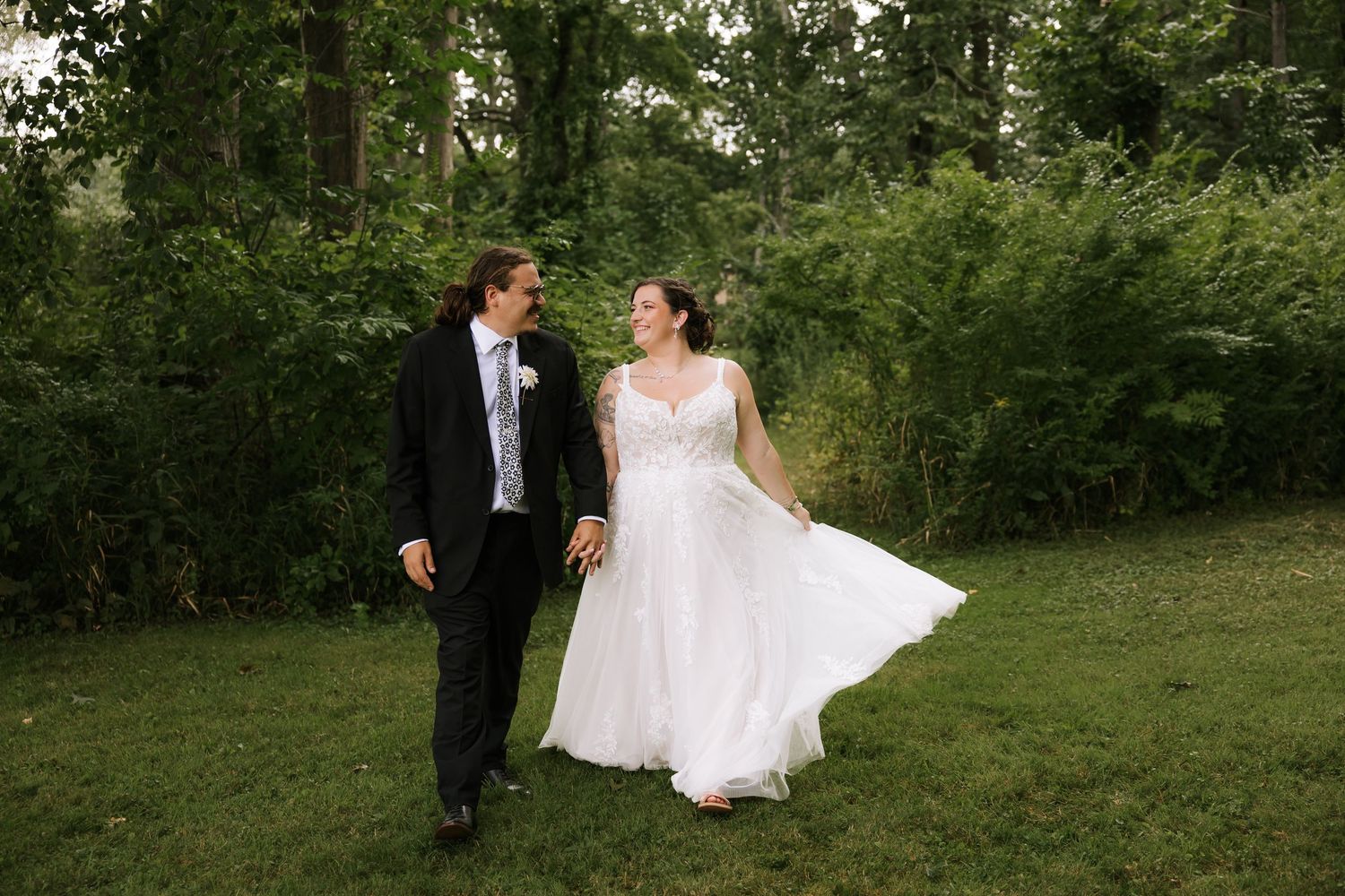 A wedding couple shares intimate moments while posing for photos in a lush green outdoor setting.