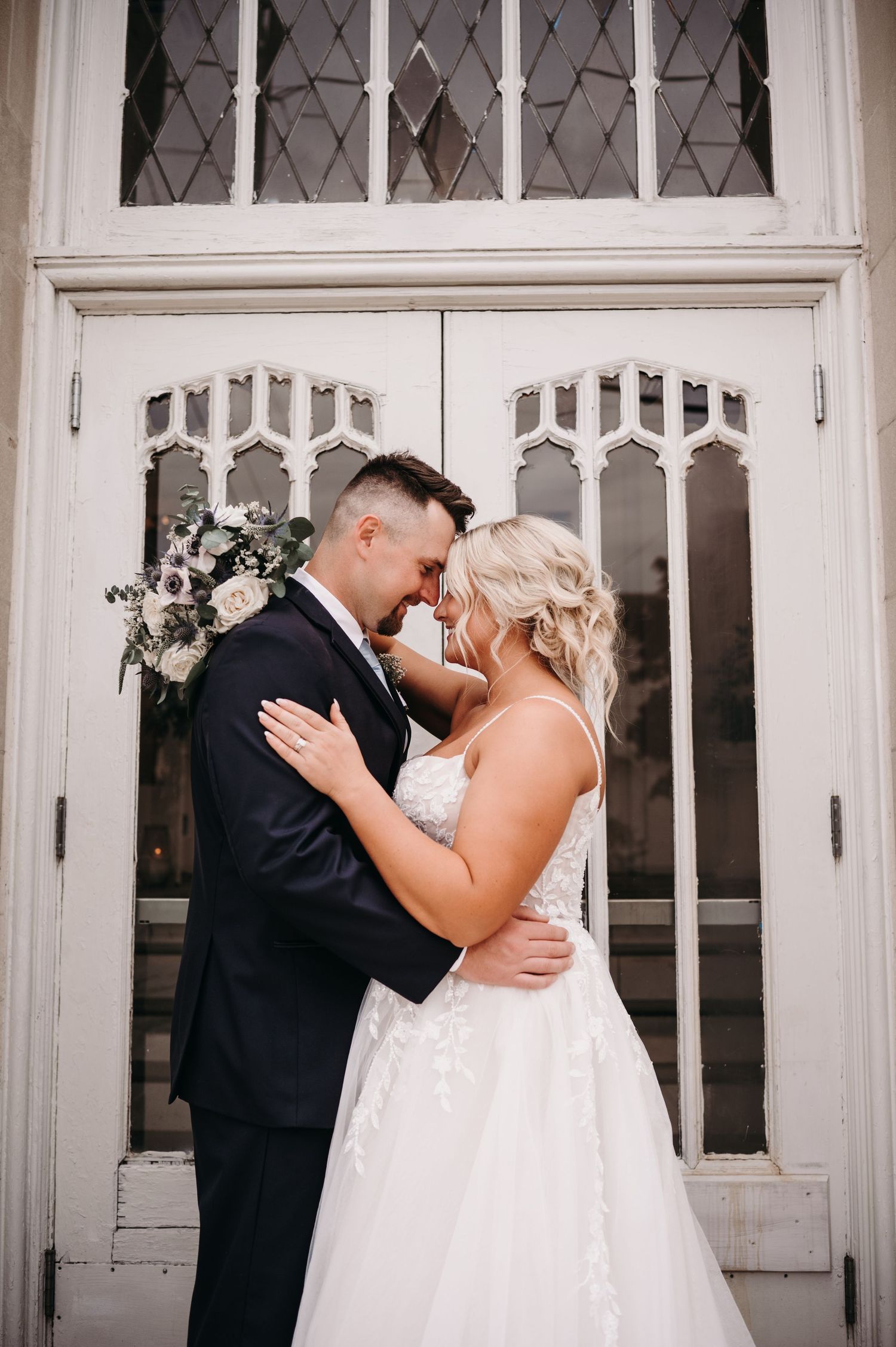 Tender moment between newlyweds embracing in front of white church doors.