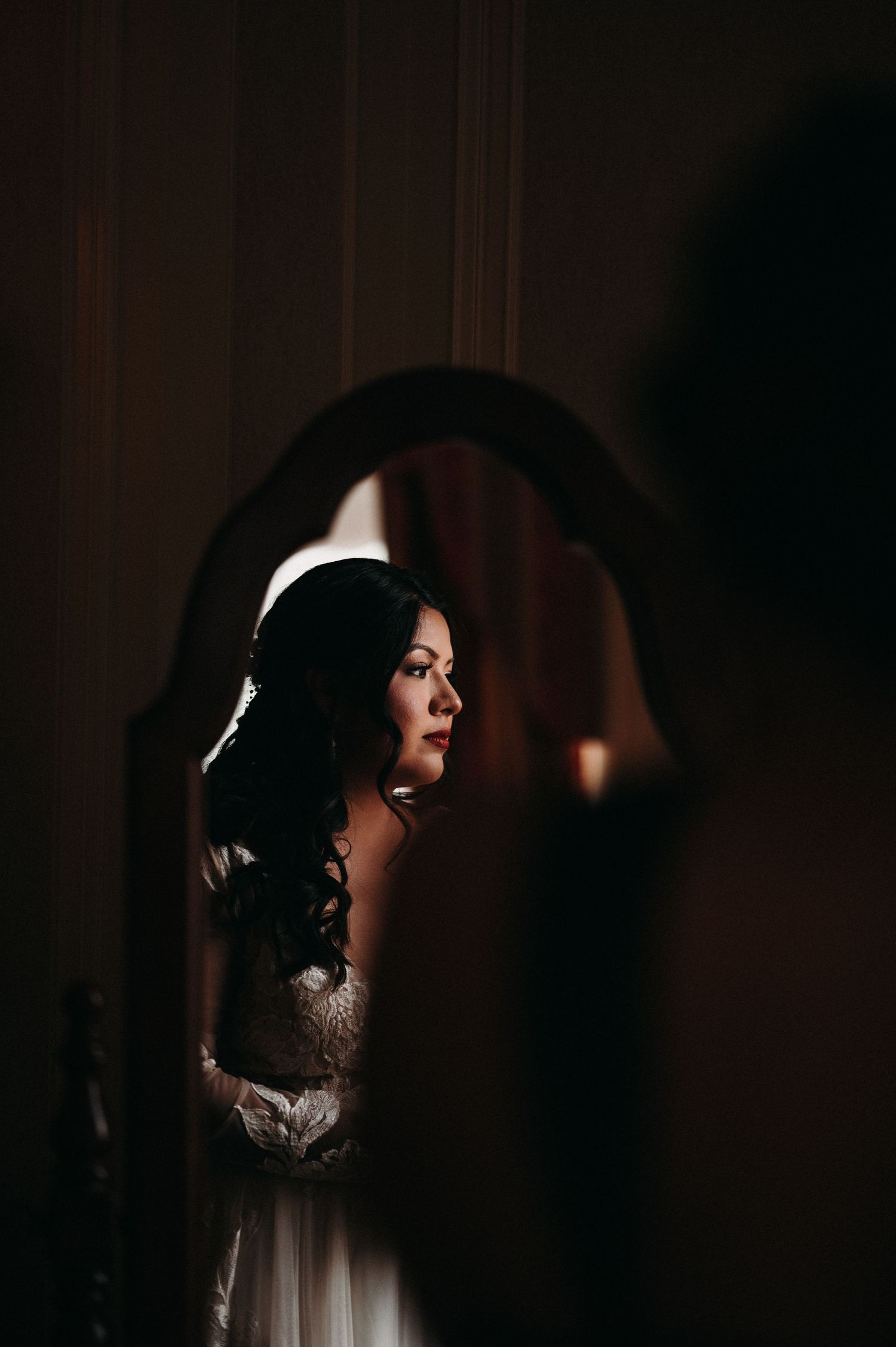 Dramatic side-lit portrait through an arched doorway shows a figure in a white dress.
