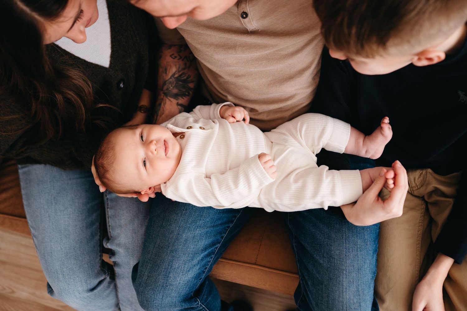 A laughing baby in white clothing lies across someone's lap on a wooden floor.