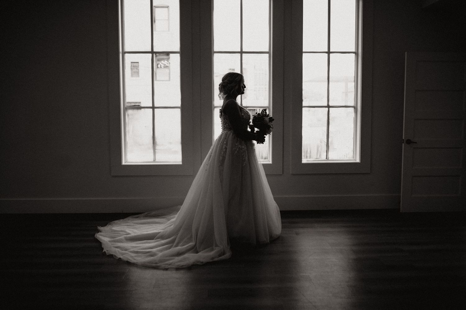 Dramatic black and white silhouette of a wedding dress against tall church windows.