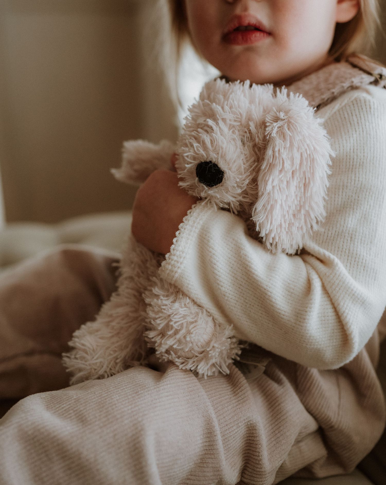 A soft plush puppy toy being held close in cozy cream sweater sleeves.