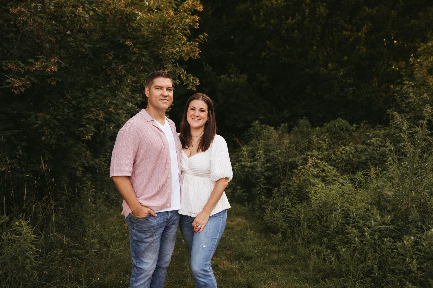 Casual outdoor family photoshoot with coordinated pink and white outfits against natural greenery.
