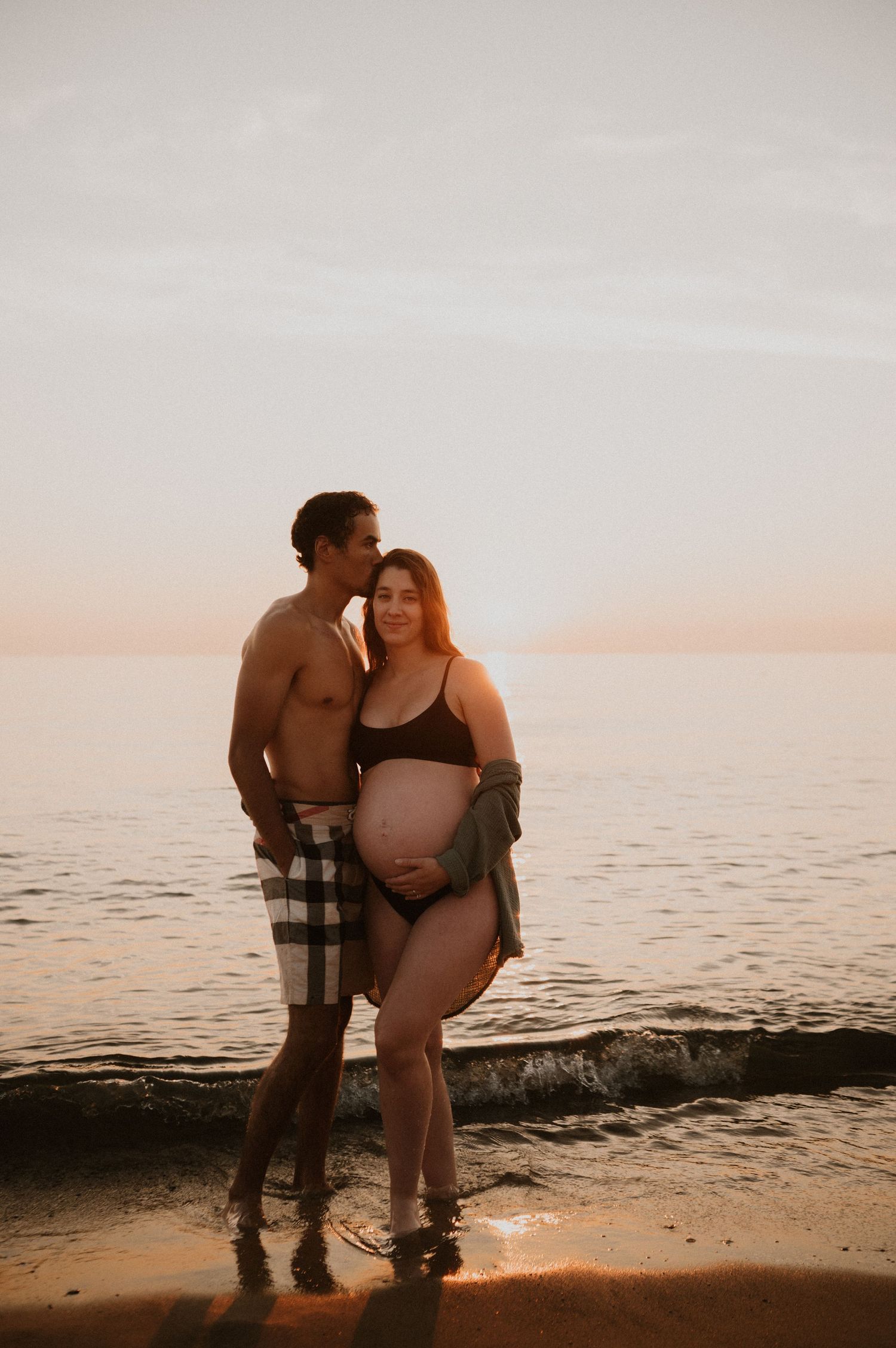 Expecting couple poses together on beach during sunset maternity photoshoot.