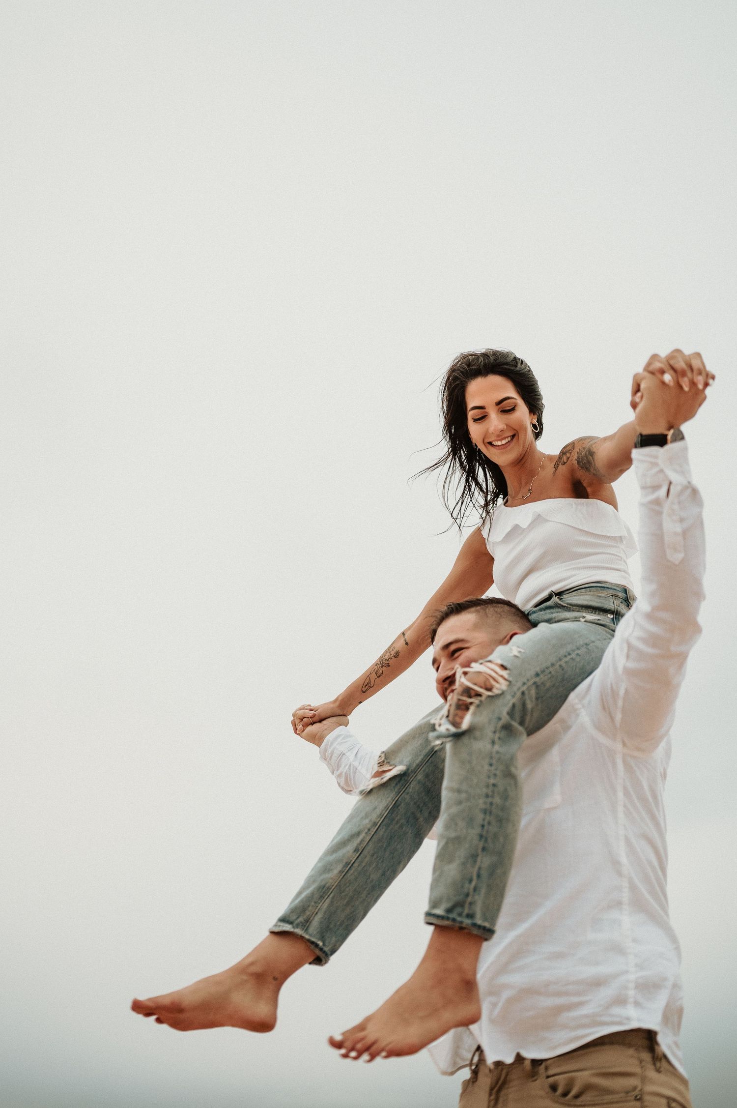 A couple plays and laughs while doing a lifting pose on sand dunes.