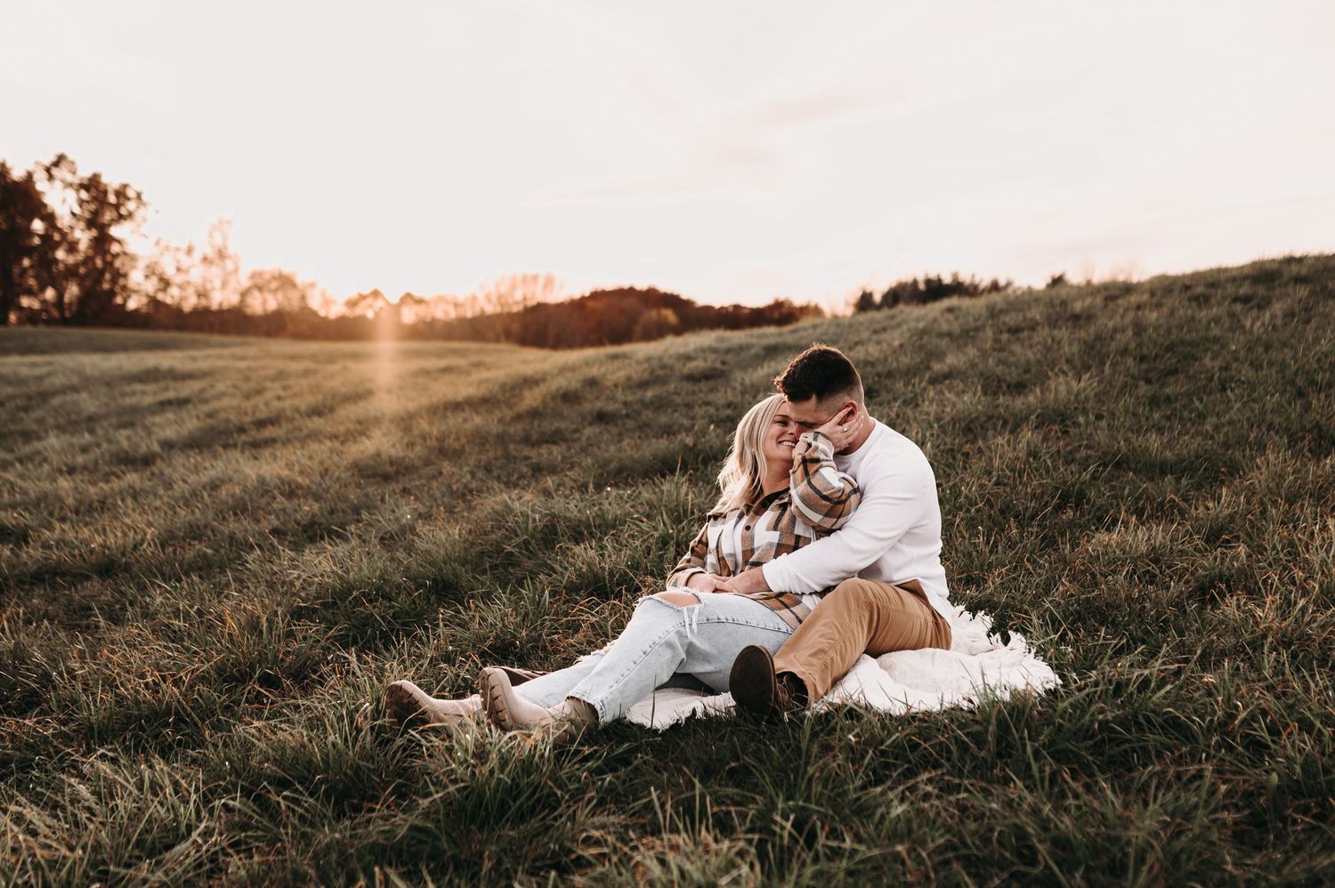 Romantic couple cuddling on white blanket in sunset meadow.
