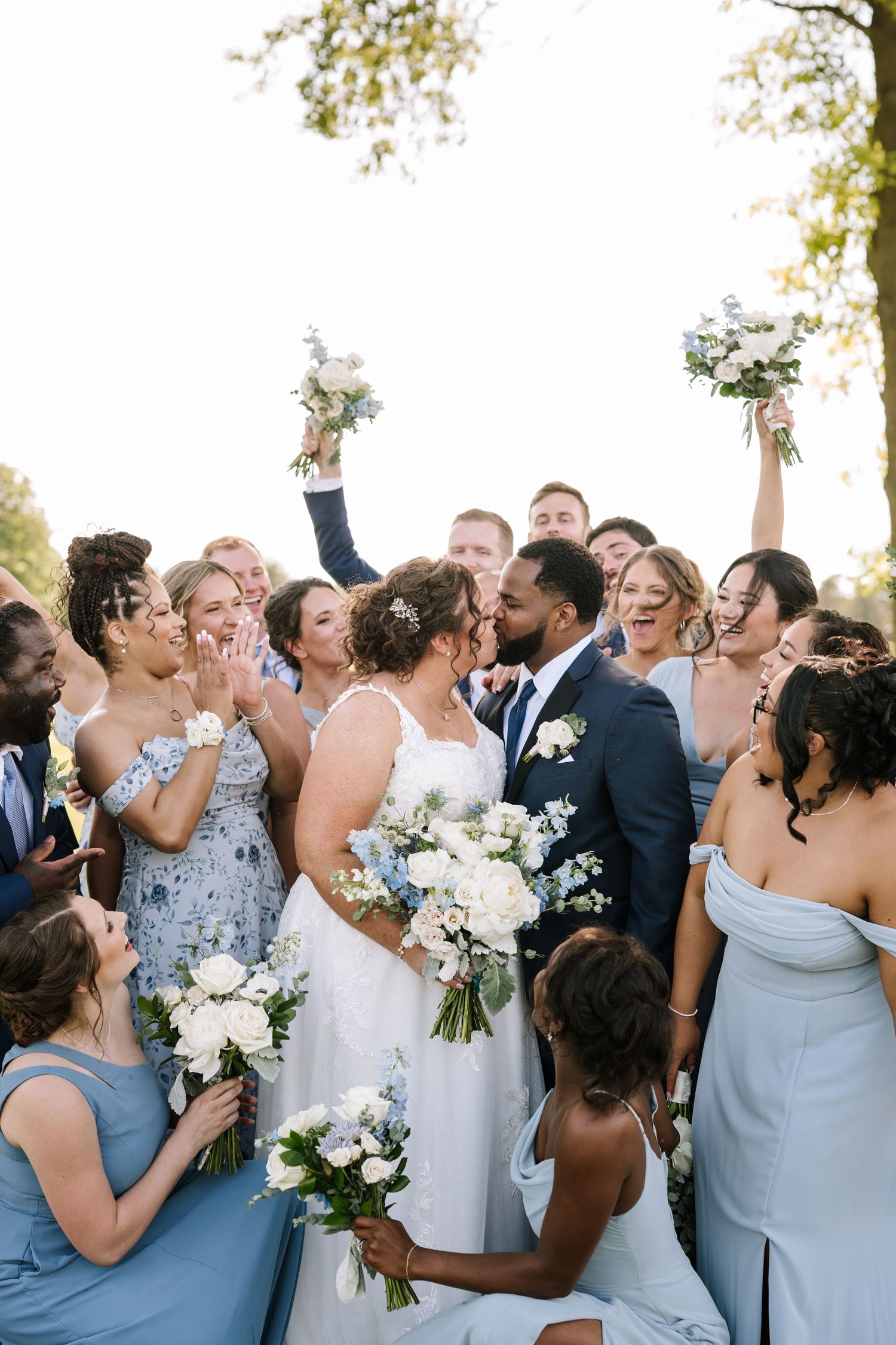 Wedding party celebrates outdoors with joyful expressions and white floral bouquets.
