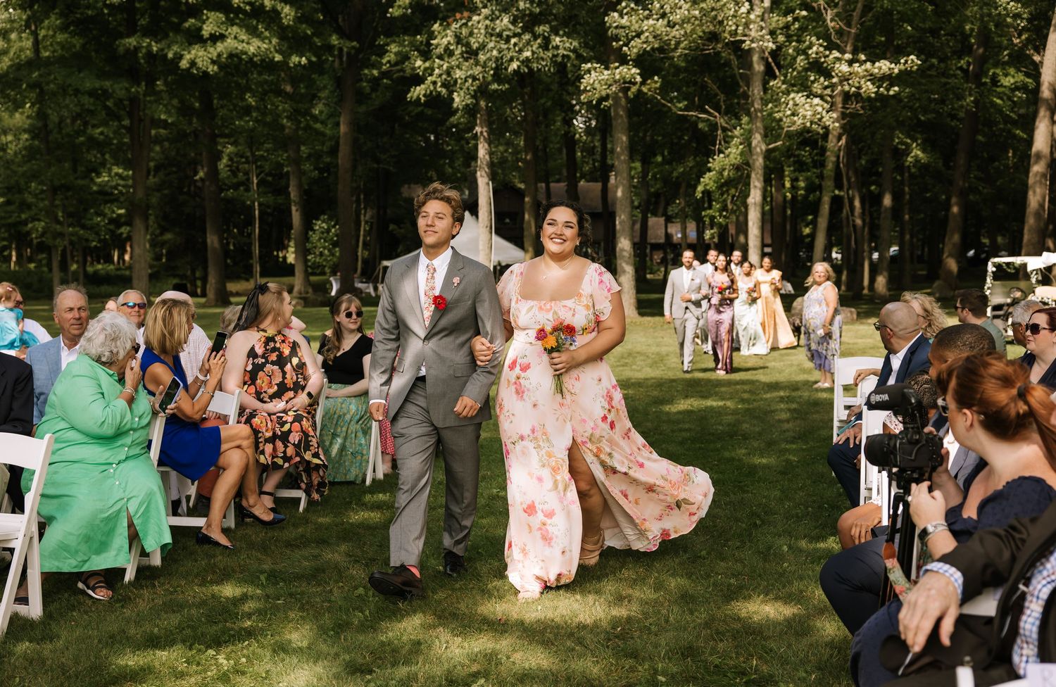 Wedding guests mingle and socialize on a lush green lawn during an outdoor summer celebration.