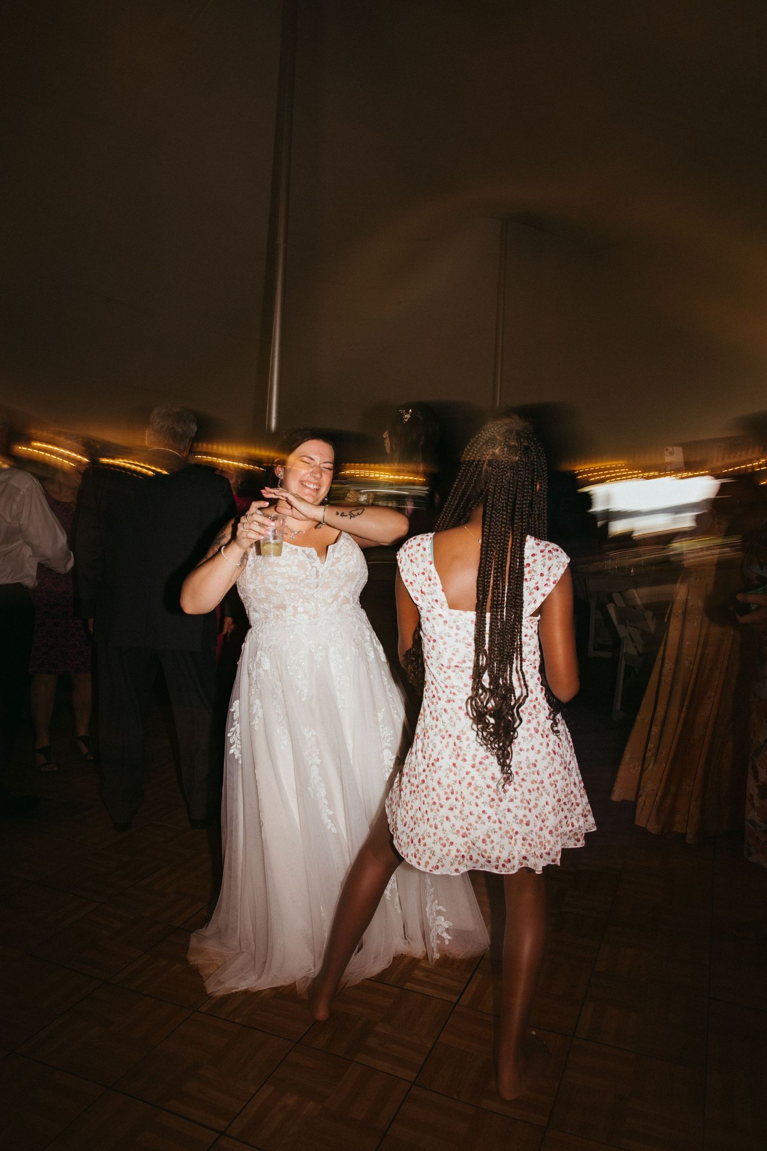 Wedding guests dancing and celebrating on a dimly lit dance floor with warm overhead lighting.