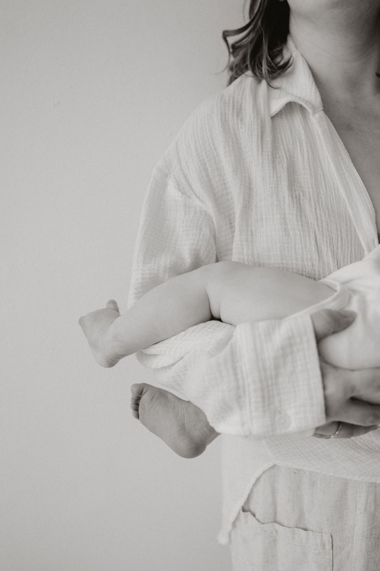 Black and white photo of mother cradling newborn baby in white linen shirt.