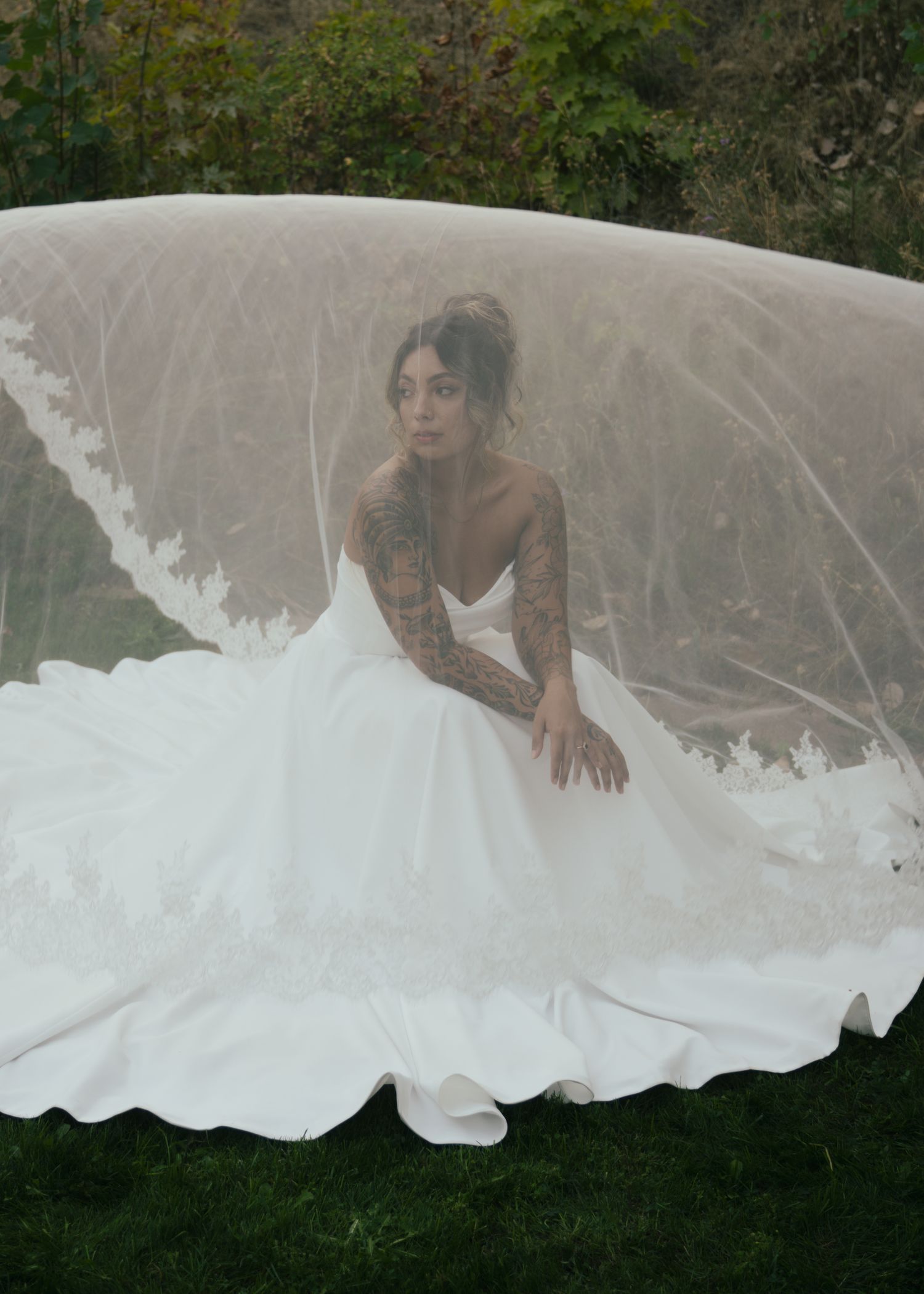 Flowing white wedding dress train spreads across green grass in artistic composition.