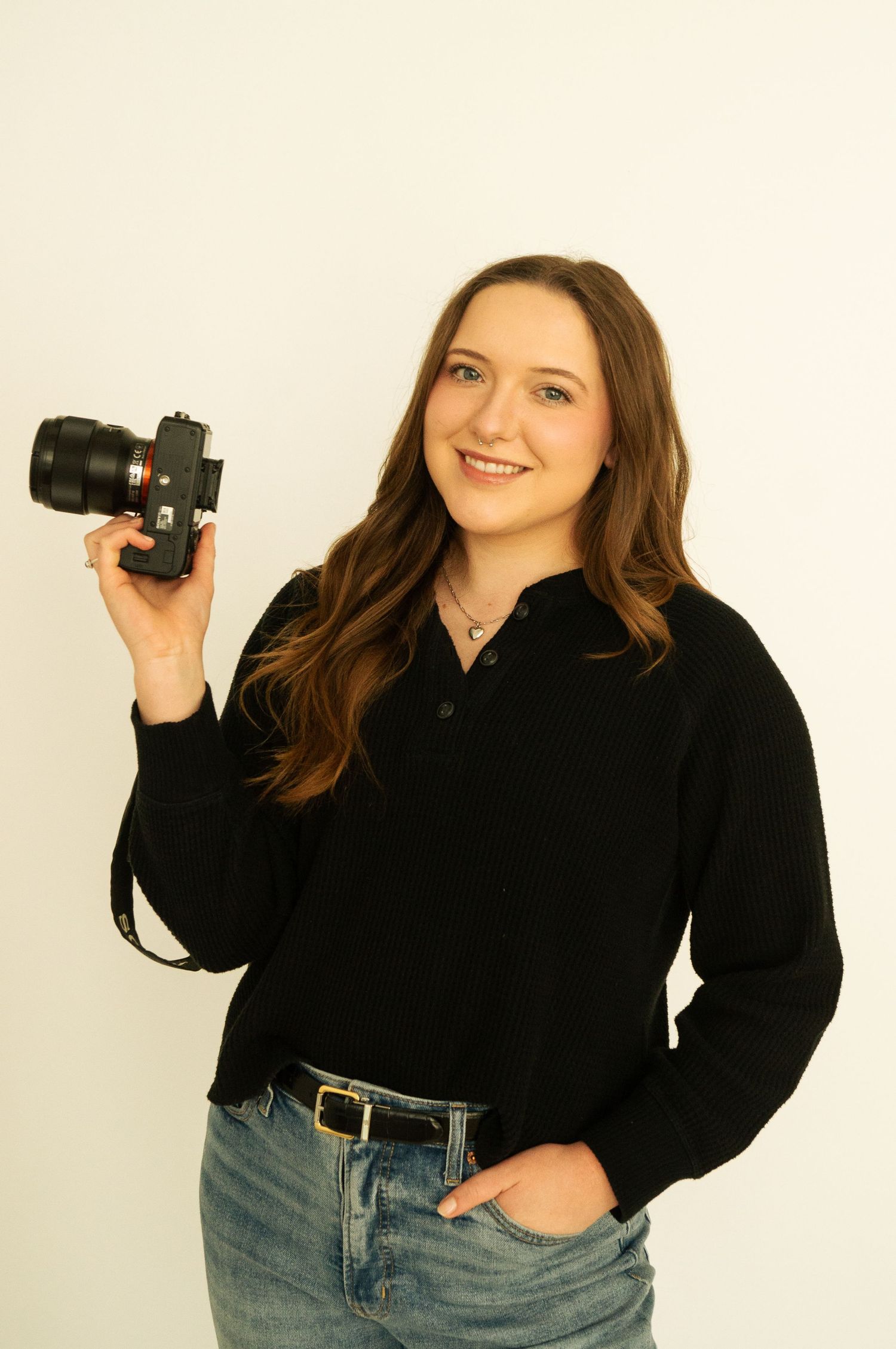 Photographer in black sweater demonstrating different poses with camera equipment.