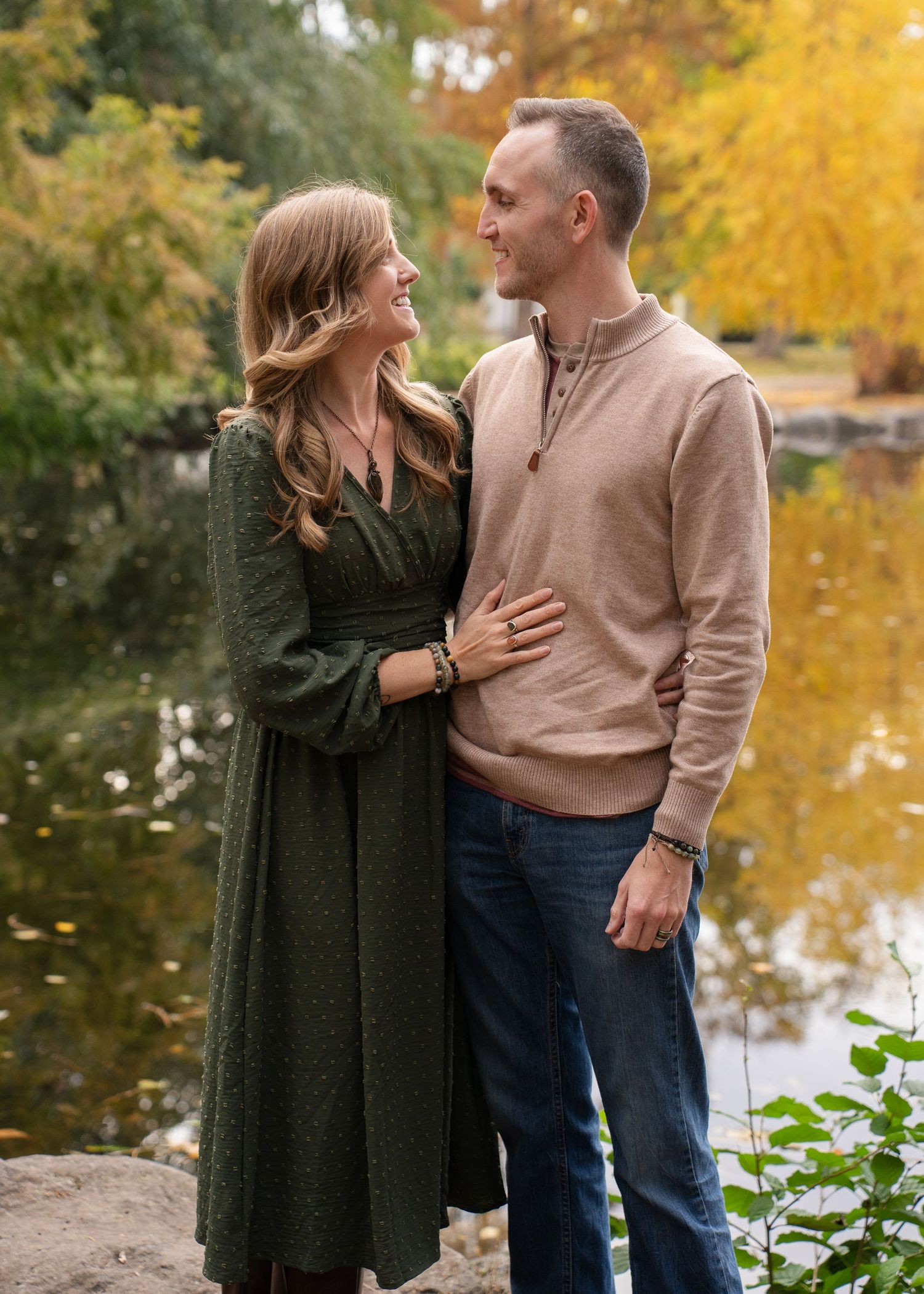 Couple shares intimate moment by autumn lake with golden foliage in background.