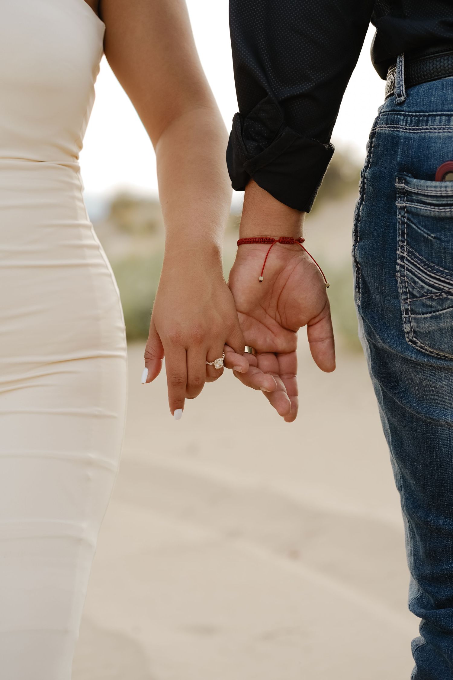 Close-up of couple holding hands, showing wedding rings and formal attire.