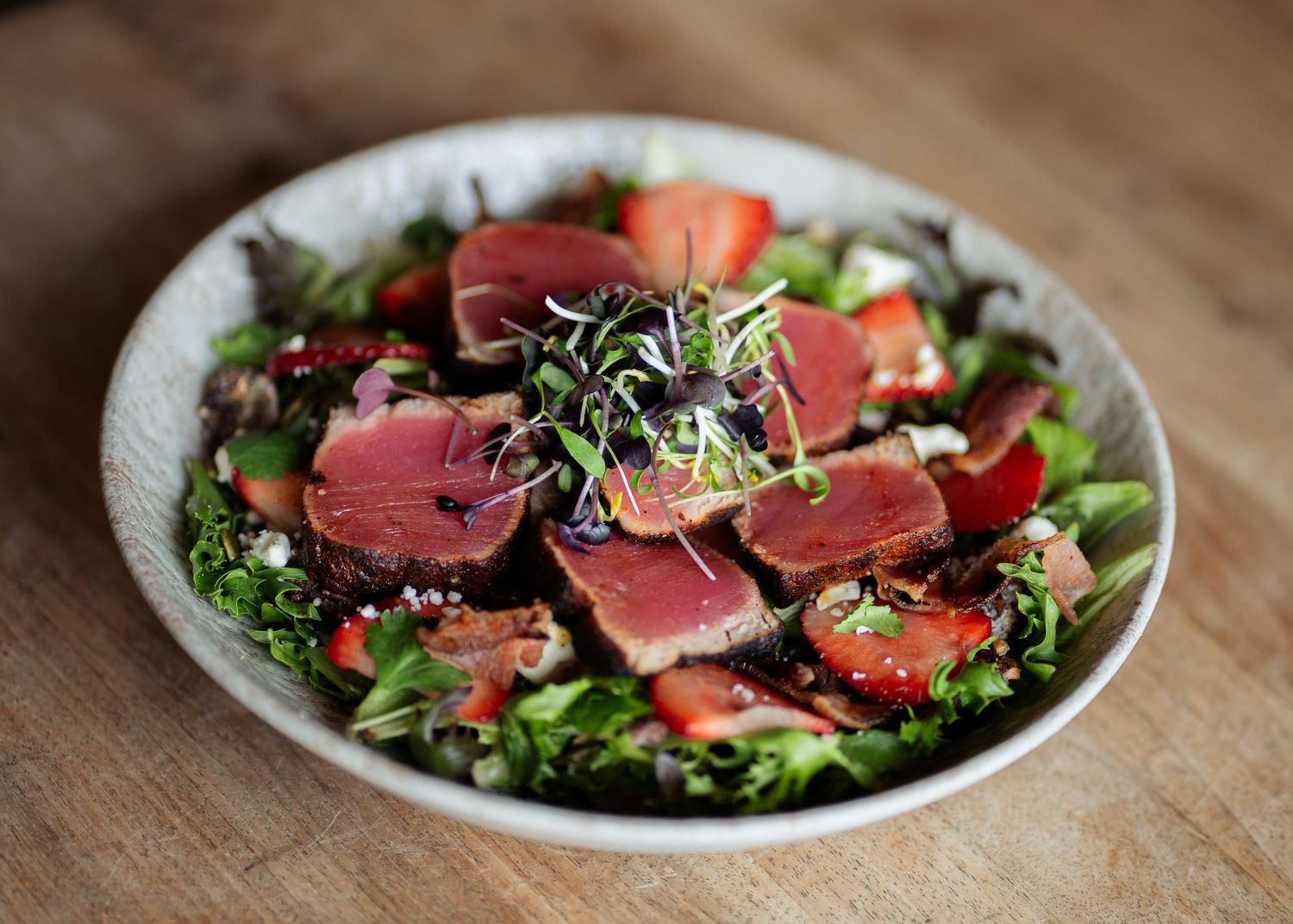 Seared tuna salad with fresh strawberries, mixed greens, and microgreens in a white bowl.