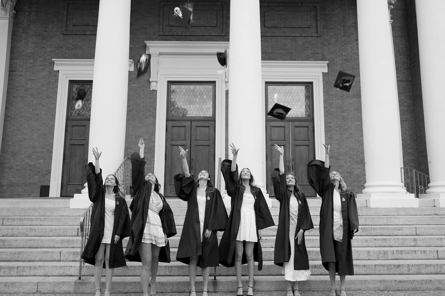 Graduates in black robes throw their caps in celebration on the steps of a columned building.
