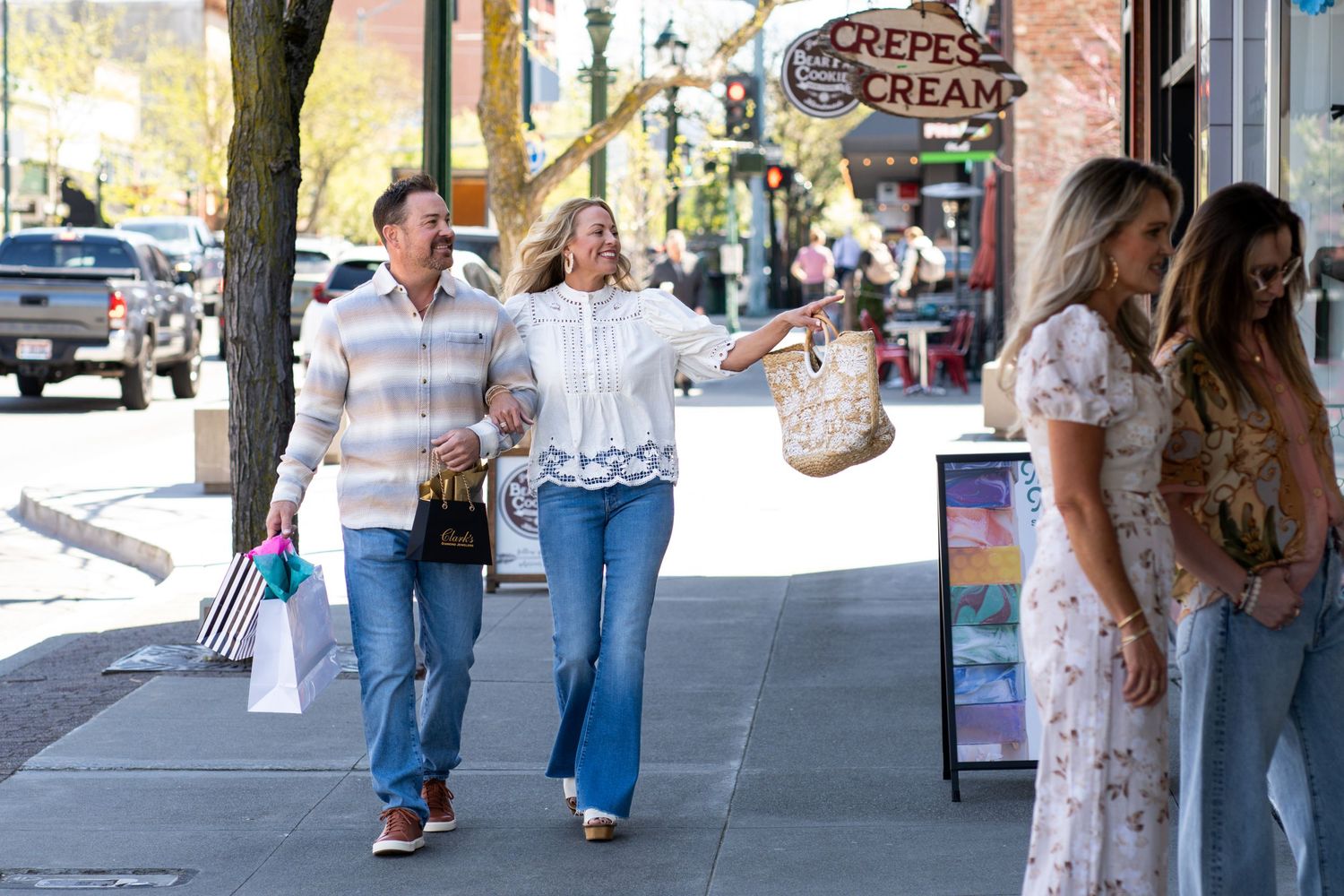 People walking along a small town sidewalk with storefronts visible in the background.