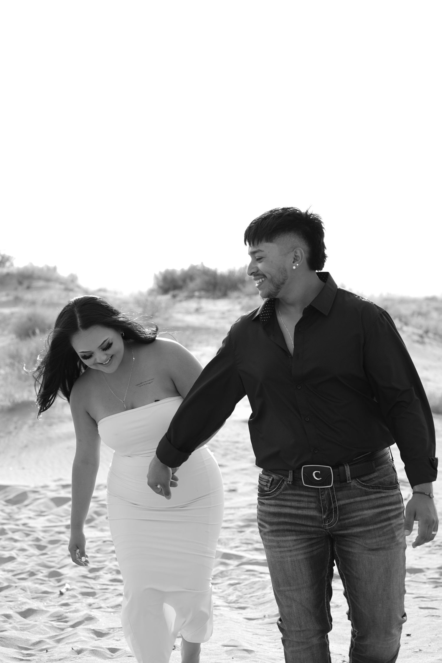 A romantic couple photoshoot on the beach showing playful moments in black and white.