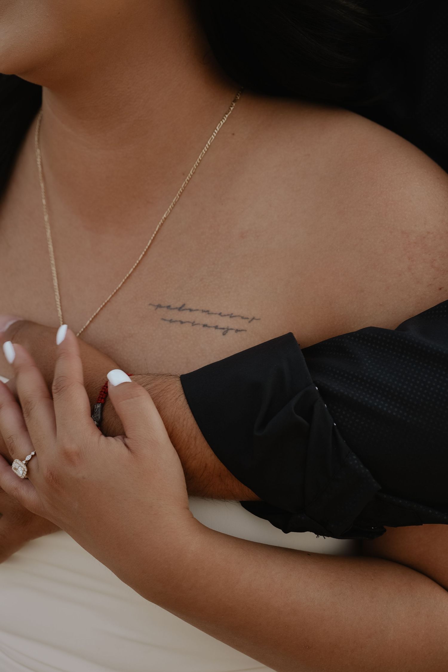 Close-up of delicate script tattoo on shoulder with silver necklace.