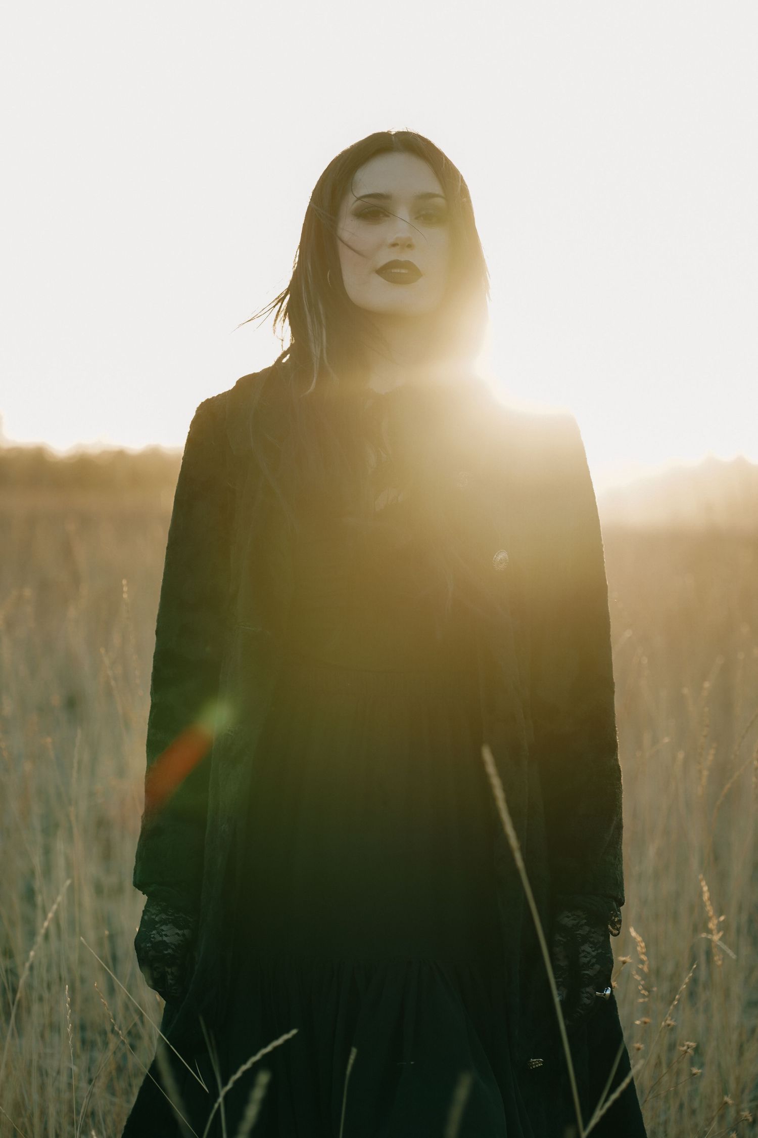 Dramatic backlit portrait in a field with sunlight creating a moody atmosphere.