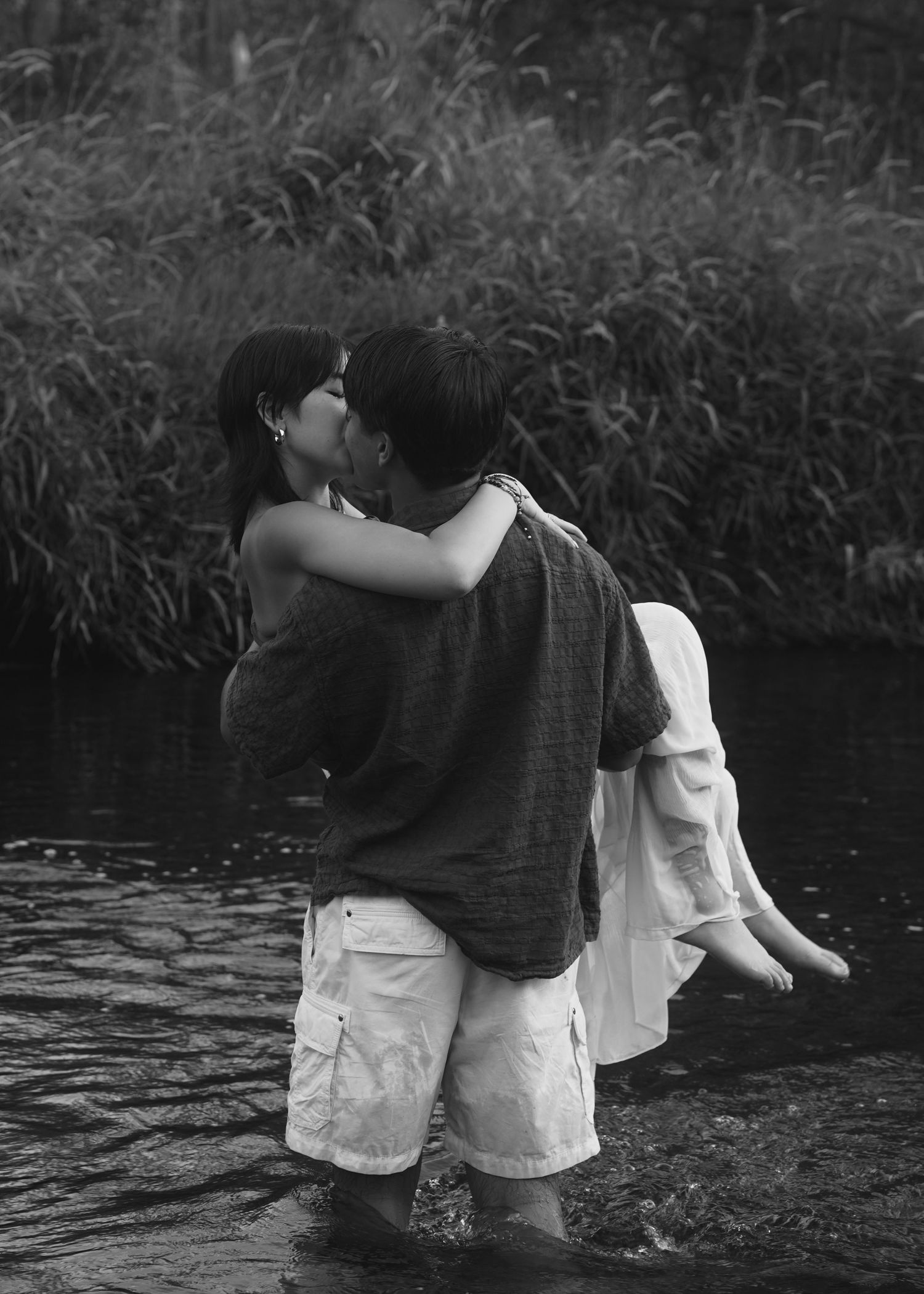 Black and white photo of couple wading together in shallow water.