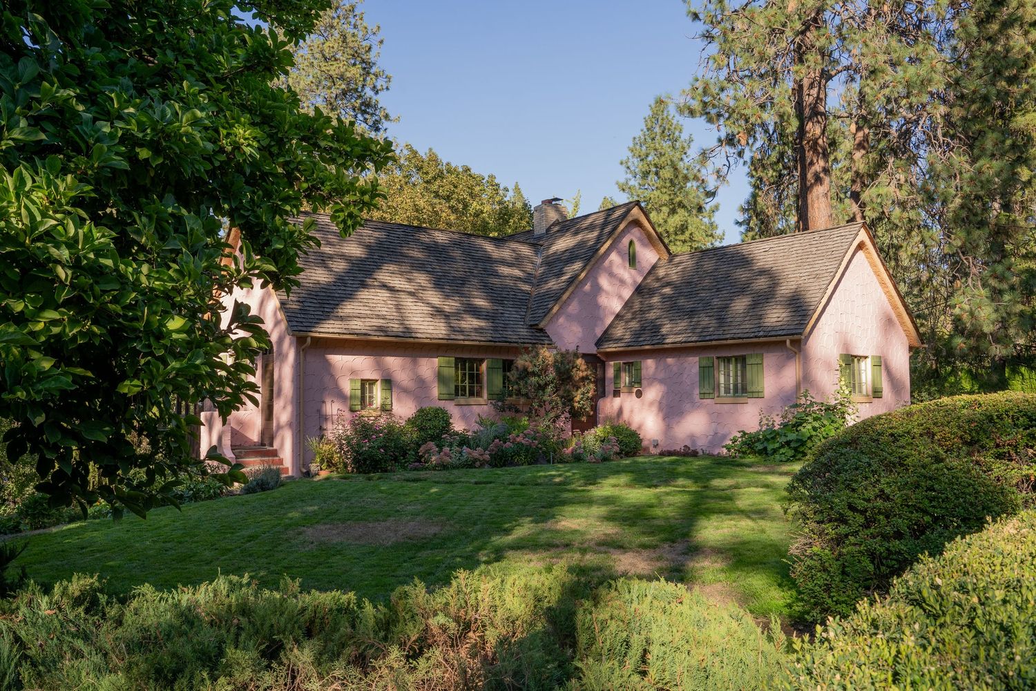 Pink cottage-style house with dormer windows nestled among trees on a green hillside.