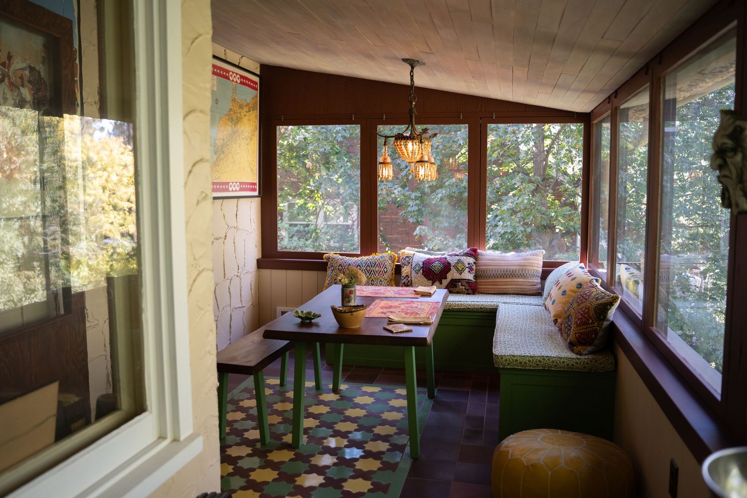 Cozy sunroom with vintage furniture, patterned floor, and large windows overlooking nature.